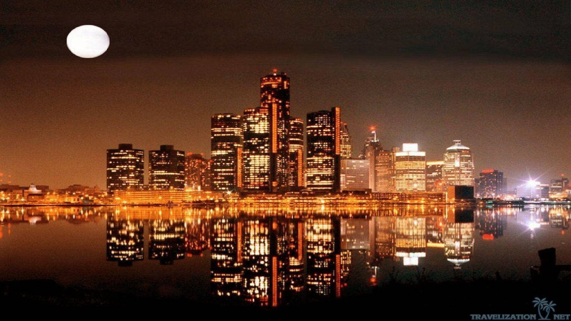 detroit 桌布 壁紙 — 一輪滿月懸掛在夜間充滿活力的城市天際線上，金色的燈光完美地倒映在平靜的水面上。