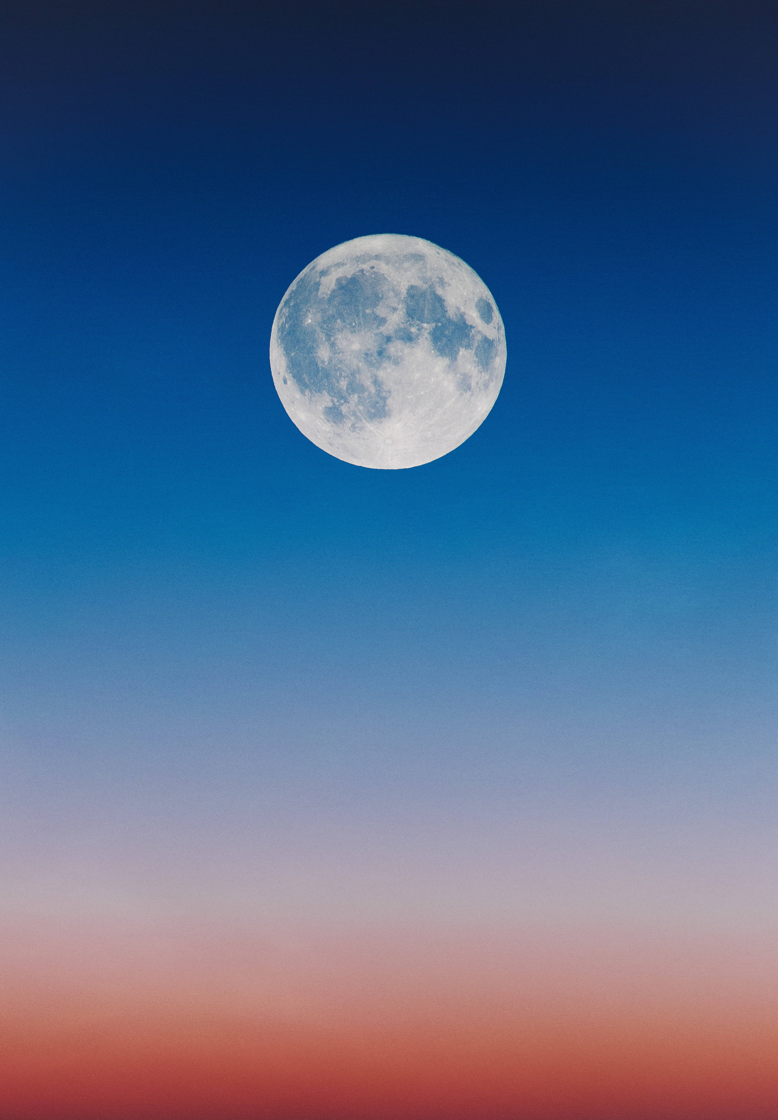 moonlight 4K 桌布 壁紙 — 一輪滿月懸掛在從深藍色過渡到地平線附近柔和粉紅色和橙色的暮色天空中。