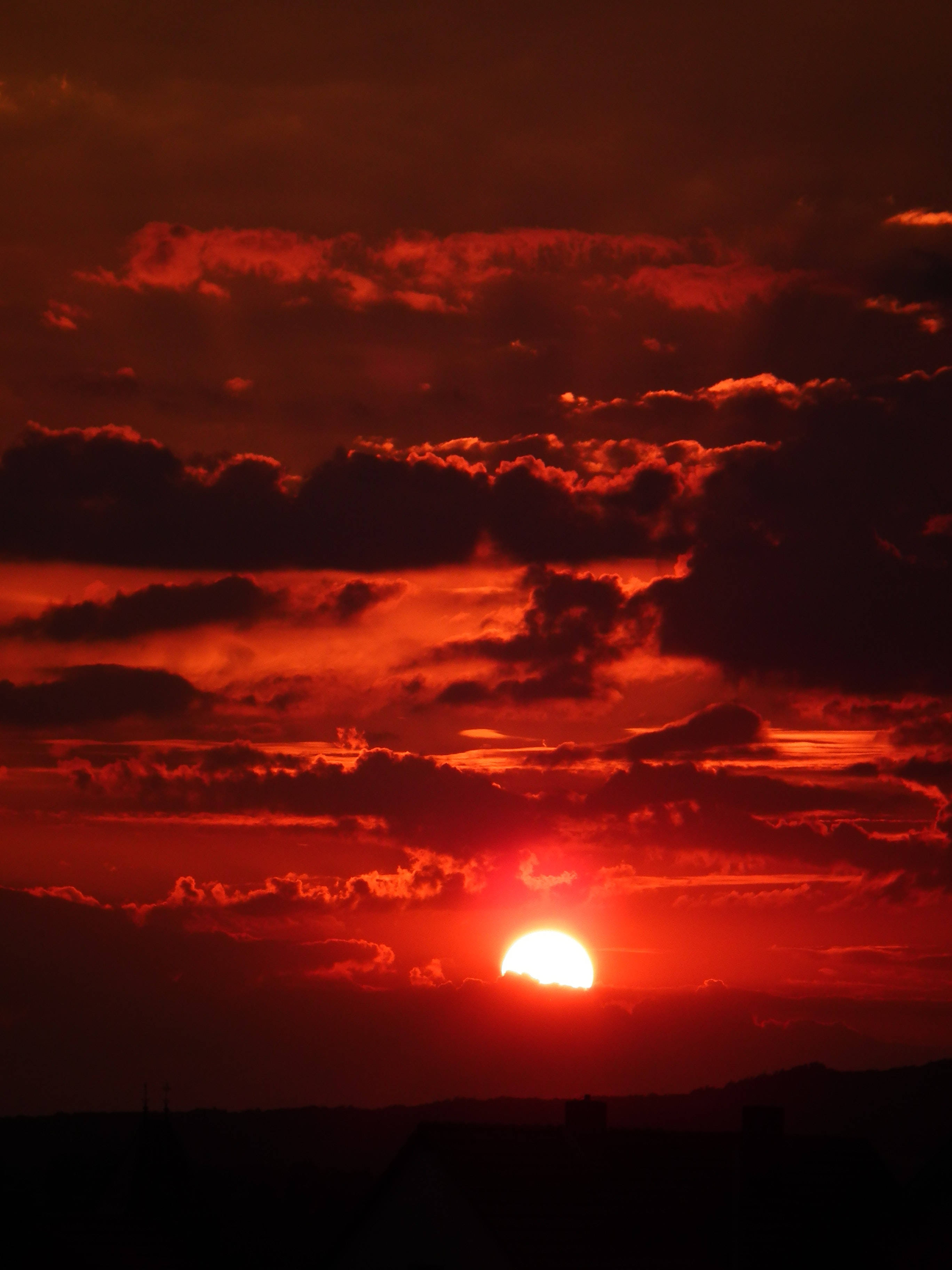 Aesthetic Sky 桌布 壁紙 — 一輪火紅的太陽在烏雲後落下，為剪影般的地平線投下強烈的光芒。
