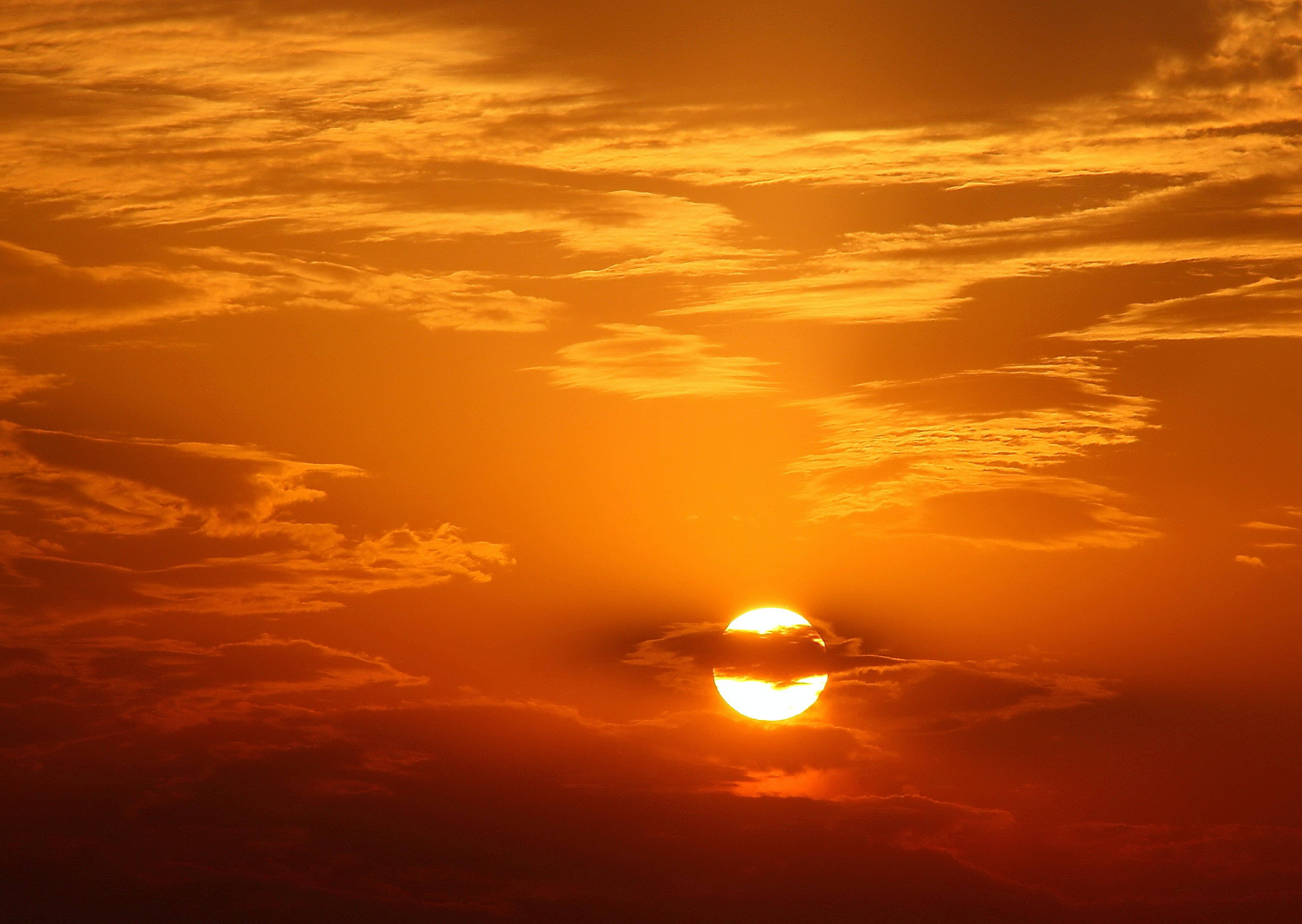 太陽 桌布 壁紙 — 一輪火紅的橙色太陽在雲層後落下，為天空投下溫暖的光芒。