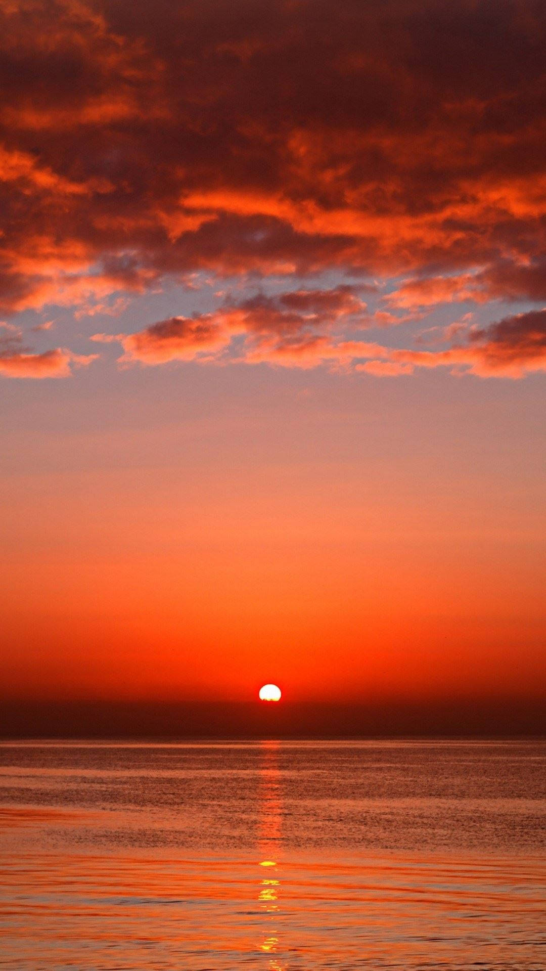 海洋上的日落，帶有火紅的橙色雲彩和寧靜的水面倒影 — 頂級 iPhone 桌布 壁紙