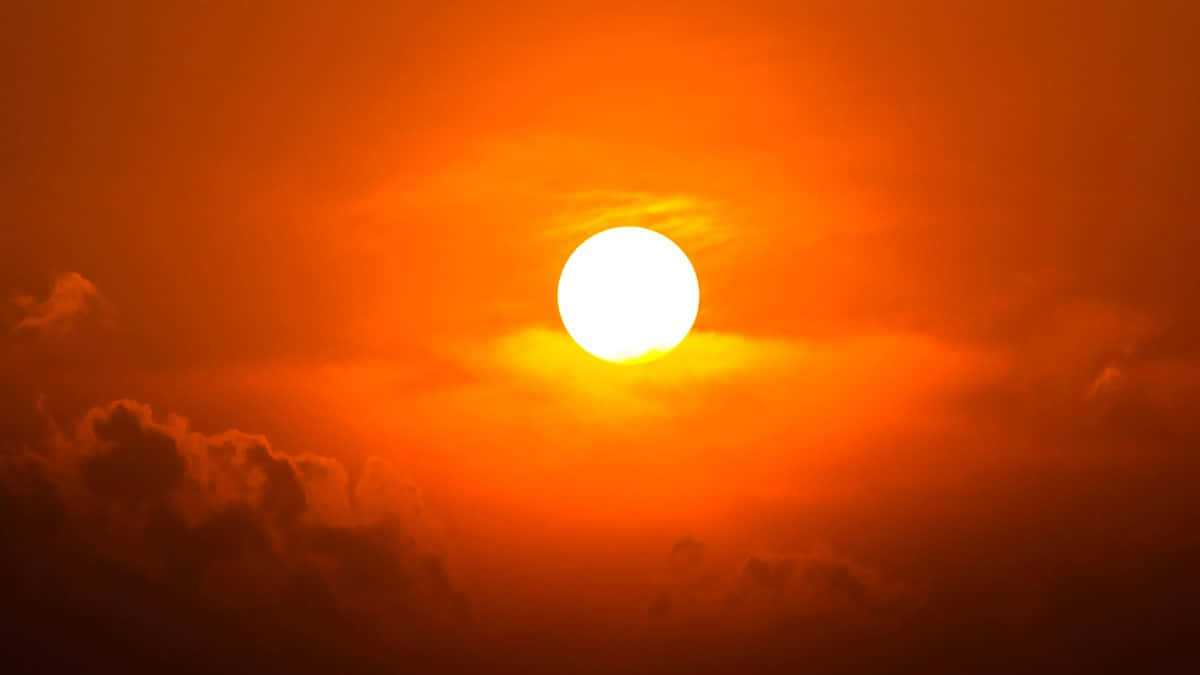 太陽 桌布 壁紙 — 一輪熾熱的太陽主宰著火橙色的天空，下方有烏雲，散發出溫暖的光芒。