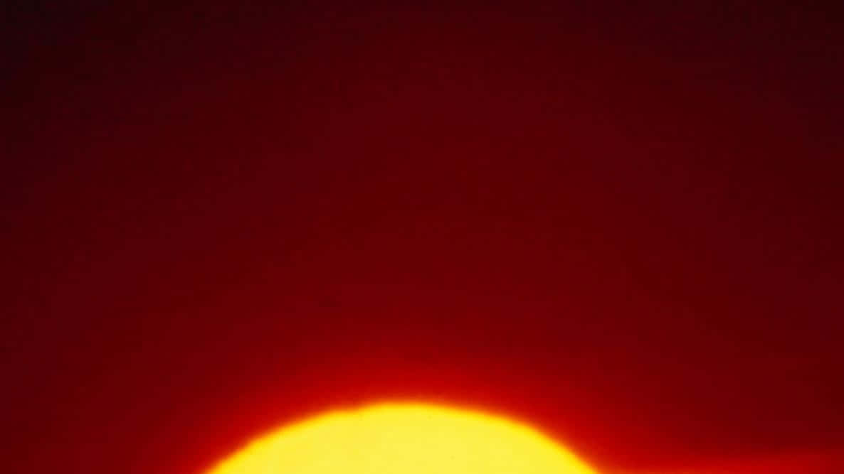 太陽 桌布 壁紙 — 一輪熾熱的太陽沉入地平線下，在天空中投射出深紅色的光芒。