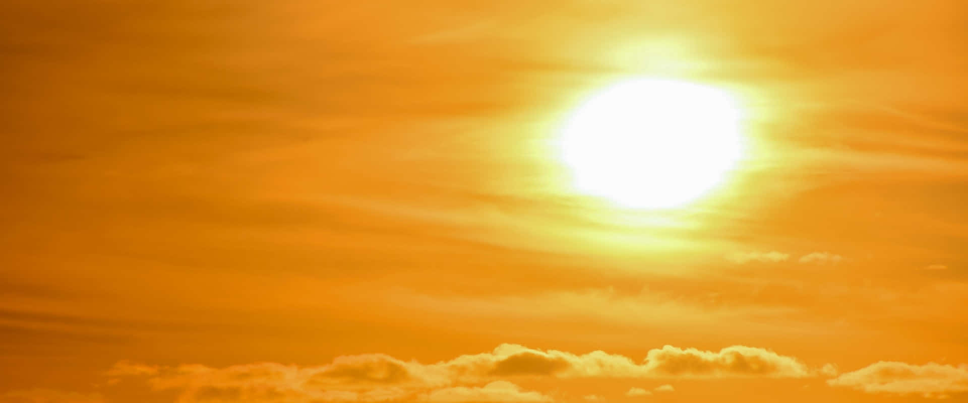 太陽 桌布 壁紙 — 一輪燦爛的太陽在溫暖的橙色天空中明亮地燃燒，下方有縷縷薄雲。
