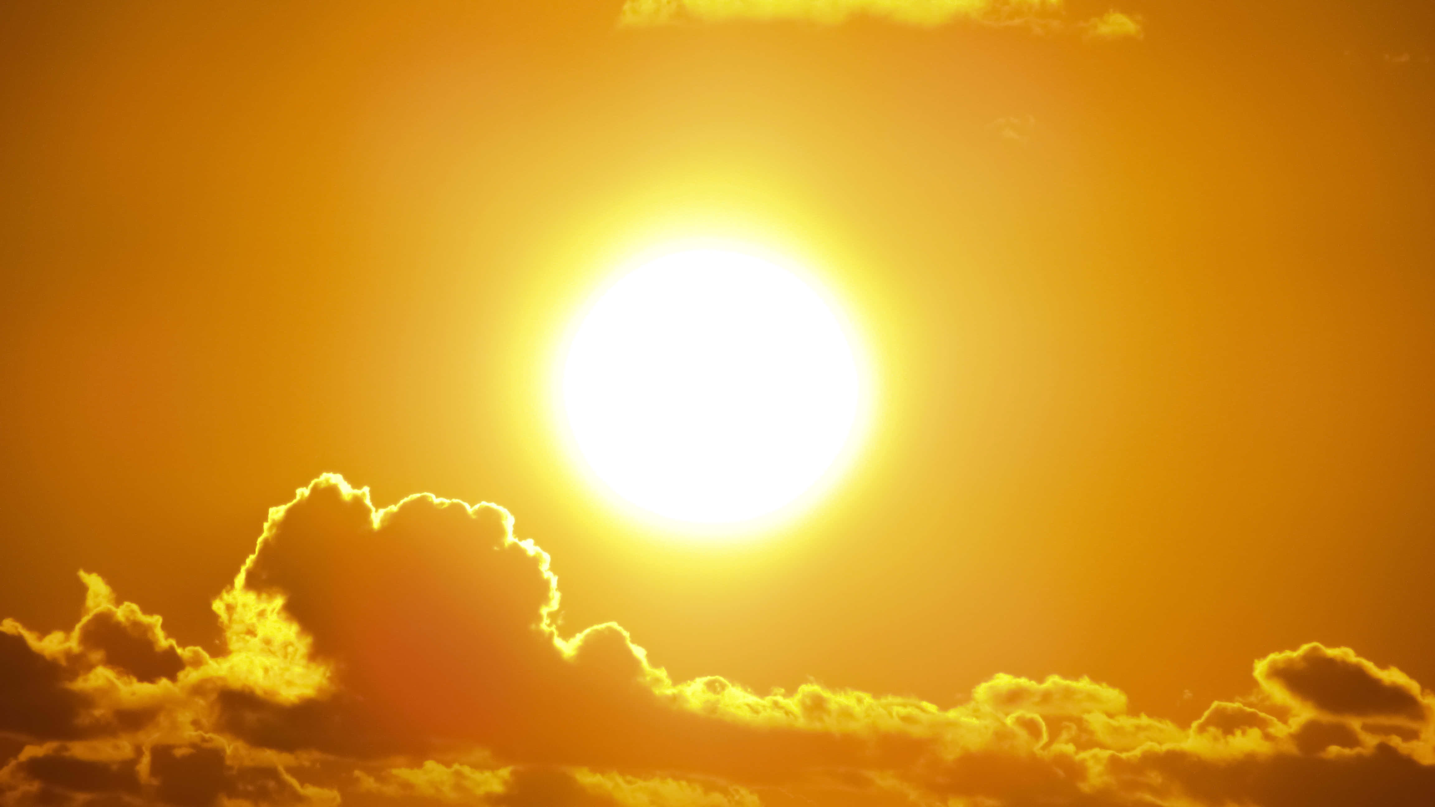 太陽 桌布 壁紙 — 一輪燦爛的太陽穿過金橙色天空，將熾熱的光芒投射在下方戲劇性的雲層上。