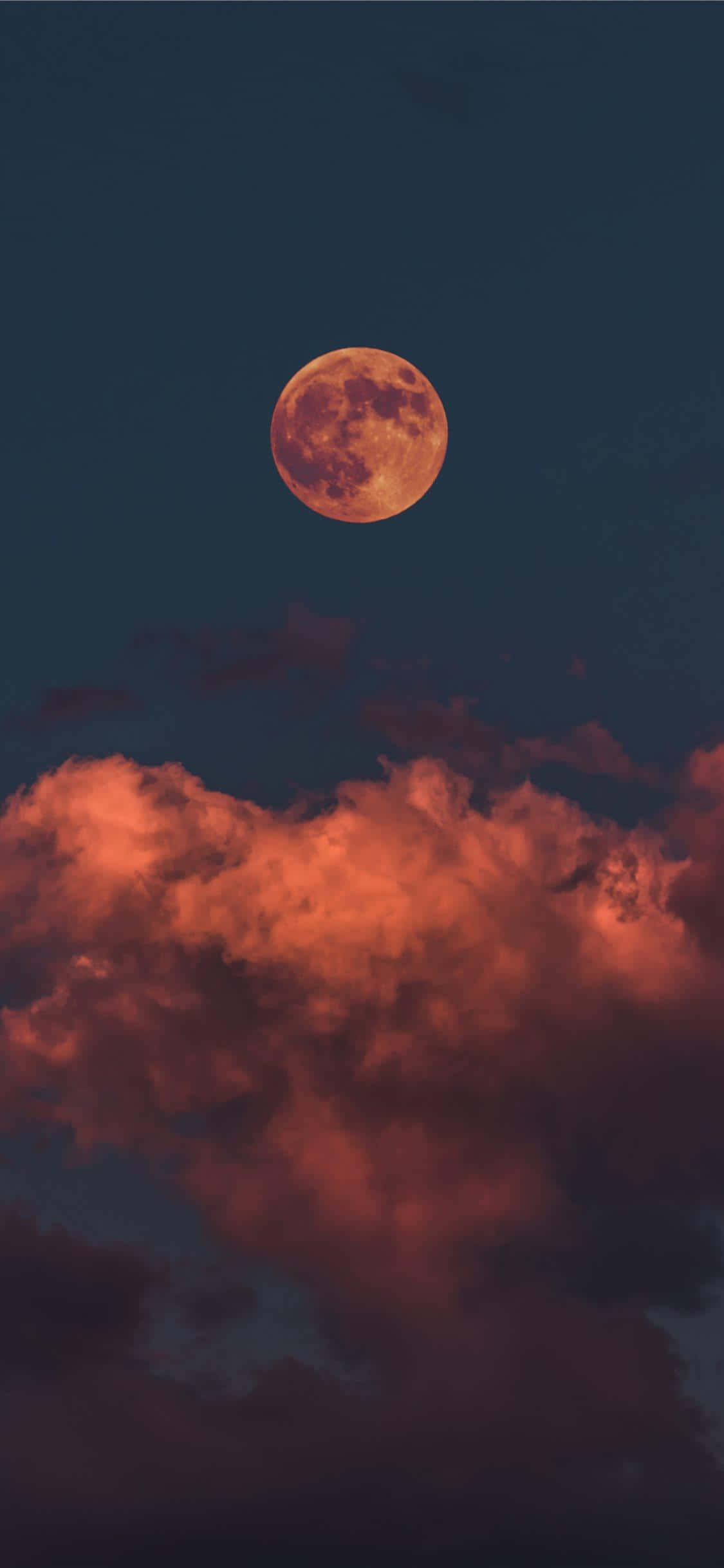 月夜星空 桌布 壁紙 — 一輪發光的橙色月亮懸掛在火紅色的雲層之上，背景是深靛藍色的夜空。