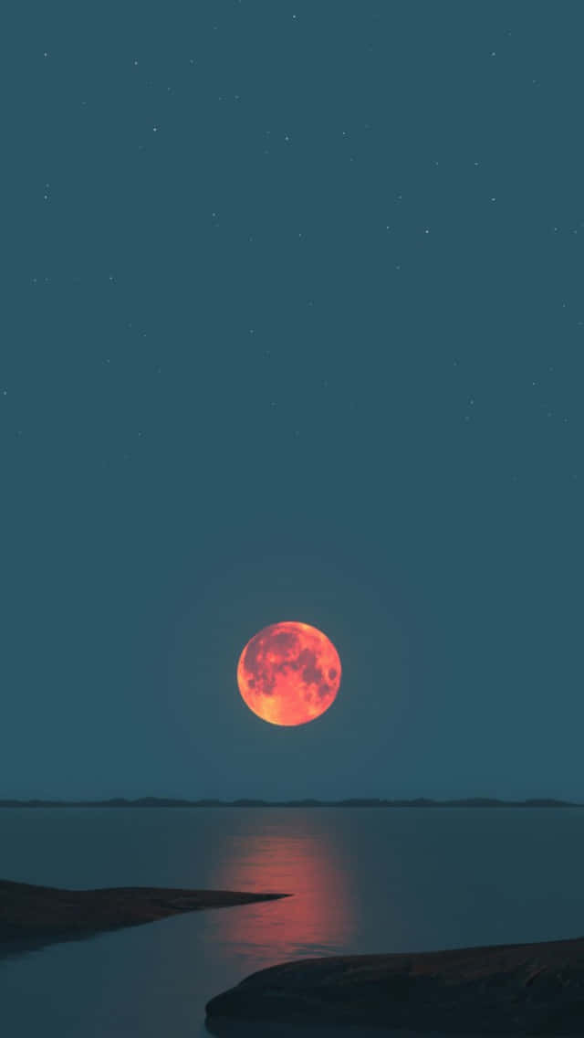Cool Moon 桌布 壁紙 — 一輪發光的紅月在繁星點點的藍綠色天空下，在平靜的水面上投下溫暖的倒影。
