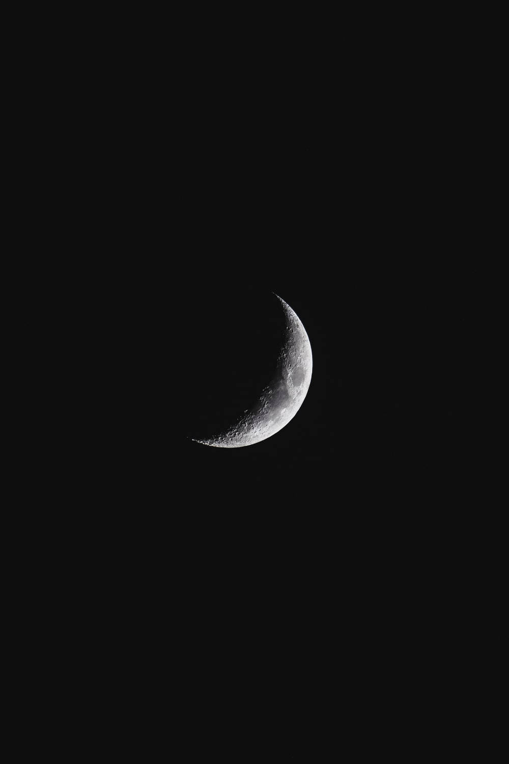 Crescent Moon 桌布 壁紙 — 一輪細節銳利的彎月在漆黑天空中發光，顯露出隕石坑和崎嶇地形。