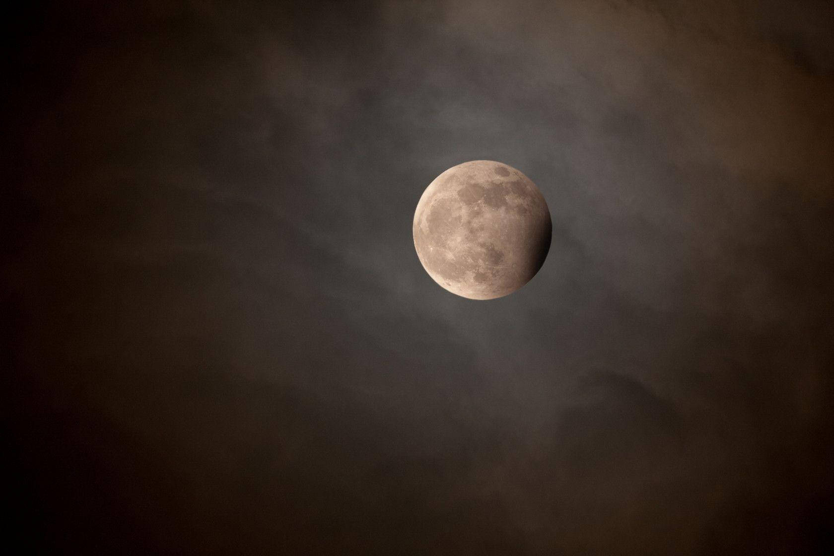 Eclipse 桌布 壁紙 — 一輪部分被遮蔽的月亮，在陰沉的夜空中透過縷縷烏雲柔和地發光。