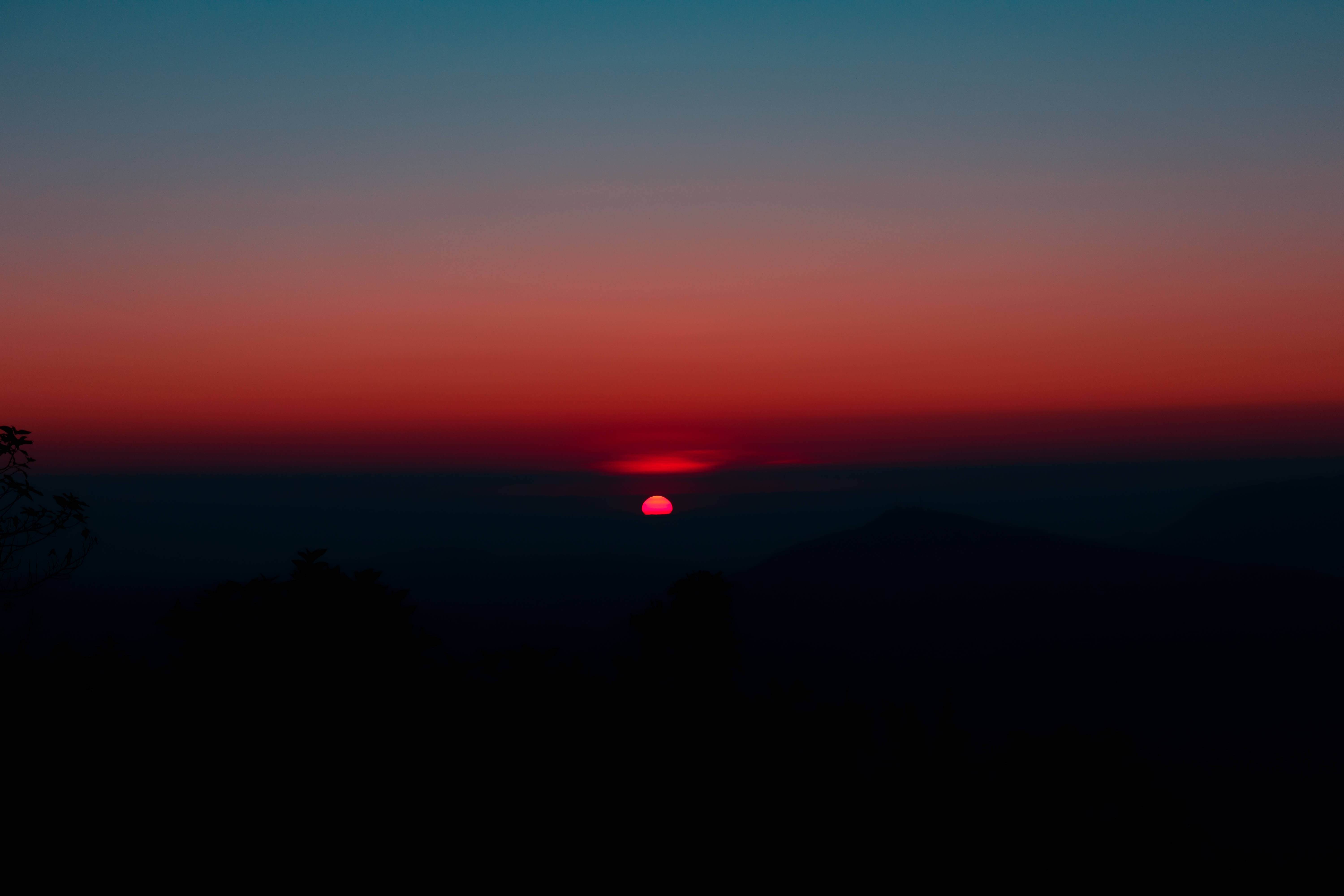 lofi 桌布 壁紙 — 一輪鮮紅的太陽沉落在遠山之下，天空由深藍漸變至火橙色。