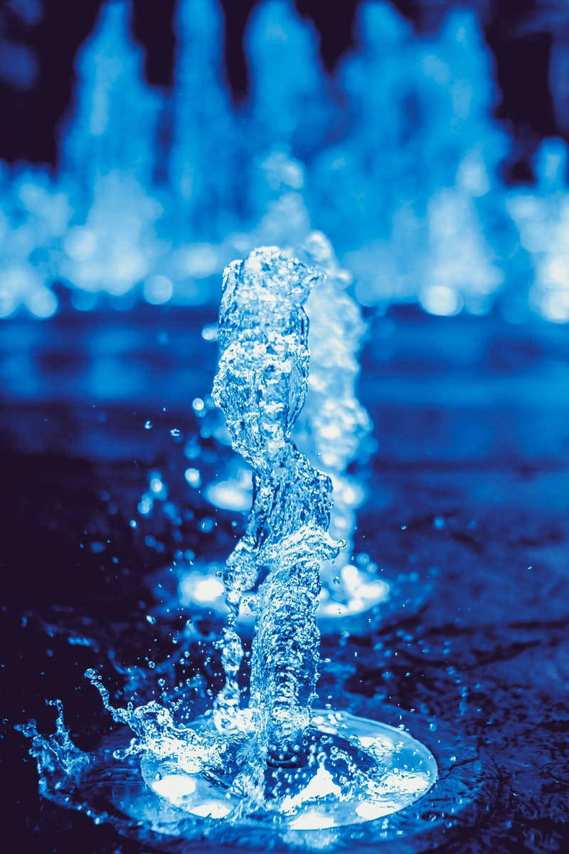 水 桌布 壁紙 — 一道充滿活力的藍色噴泉水流以清晰焦點向上拱起，背景是類似水流形成的模糊動態水景。