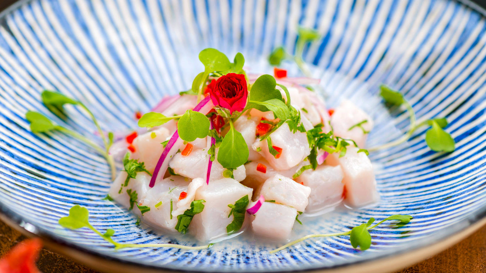 魚 桌布 壁紙 — 一道充滿活力的酸橘汁醃魚菜餚，配有切塊魚肉、微型蔬菜和紅色花朵裝飾，盛在藍色條紋碗中。