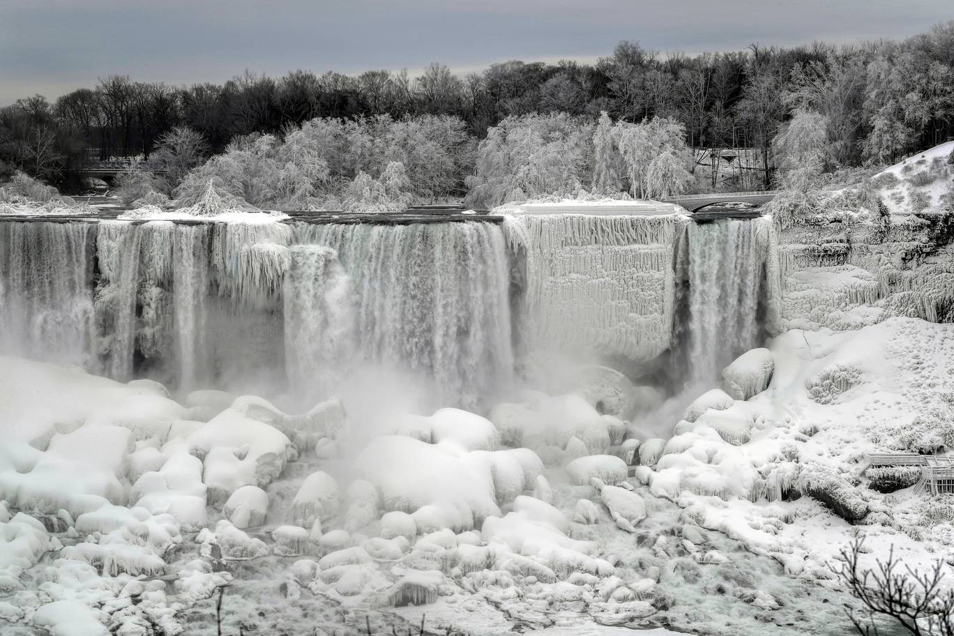 niagara 桌布 壁紙 — 一道冰凍的瀑布從冰崖上傾瀉而下，周圍是白雪覆蓋的樹木，天空是灰色的冬日景象。