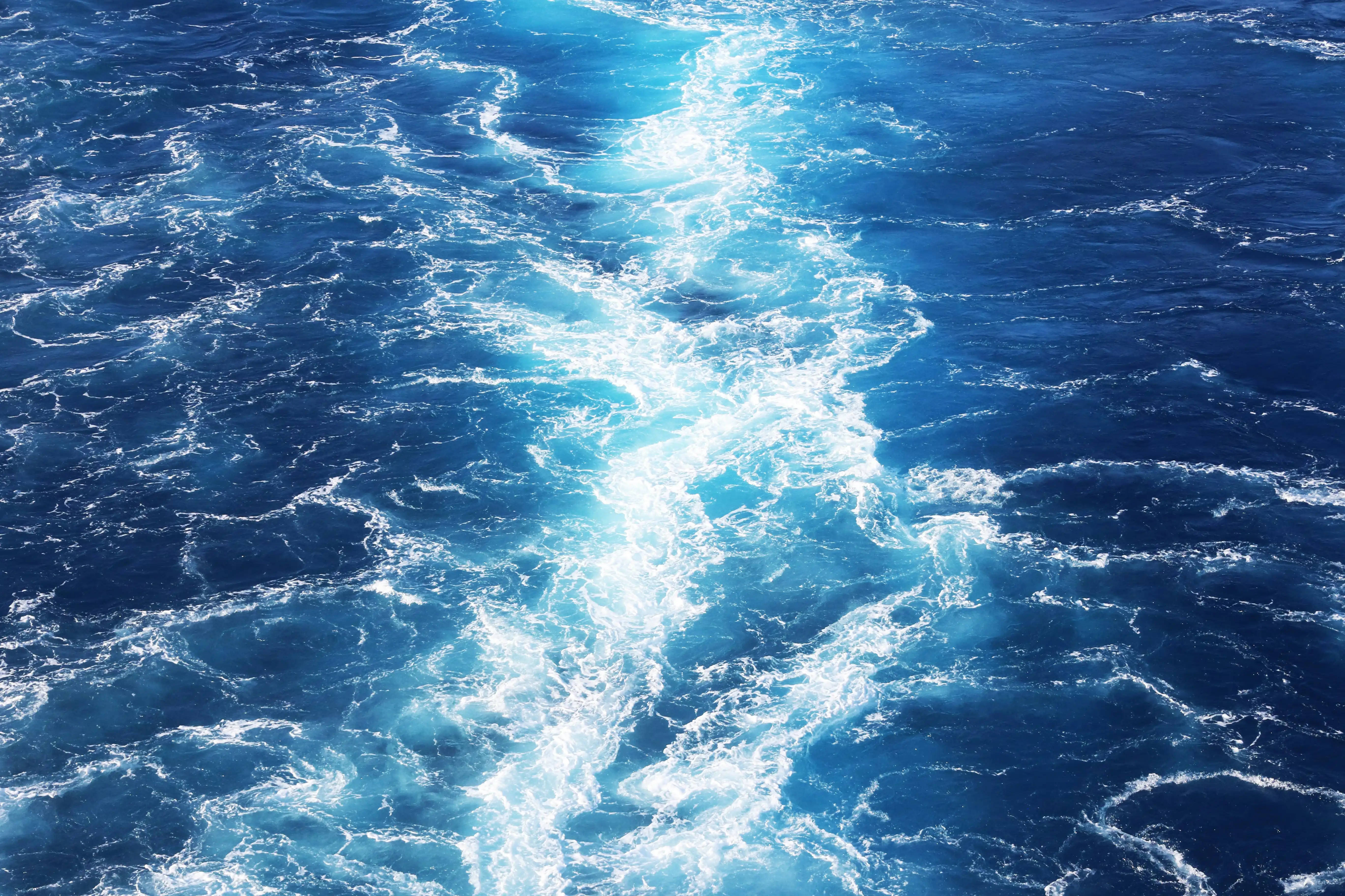 水 桌布 壁紙 — 一道動態的白色泡沫波浪痕跡在明亮的陽光下劃過深藍色的海水。