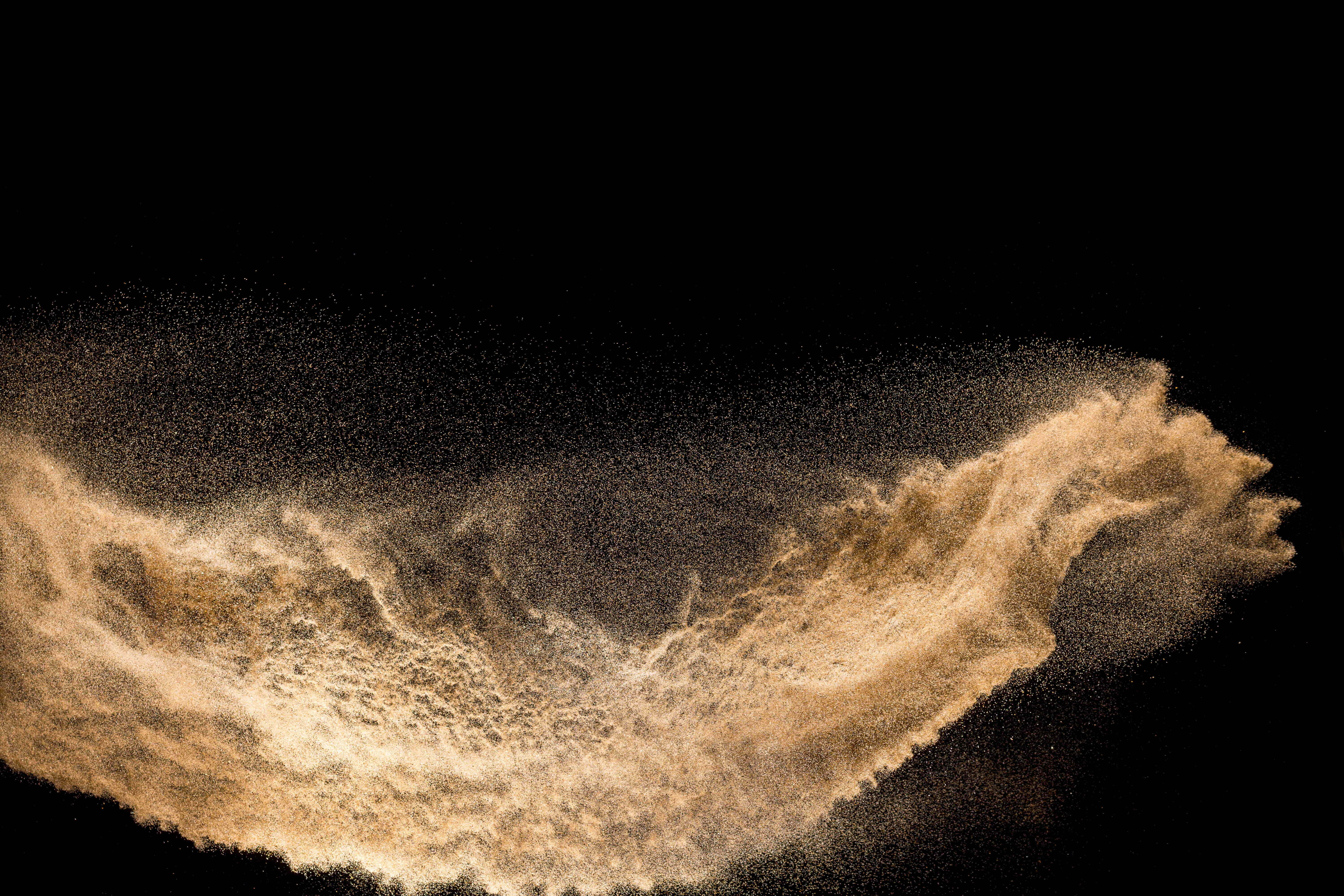 Dust 桌布 壁紙 — 一道動態的金色沙粒弧線懸浮在半空中，襯托著純黑背景。
