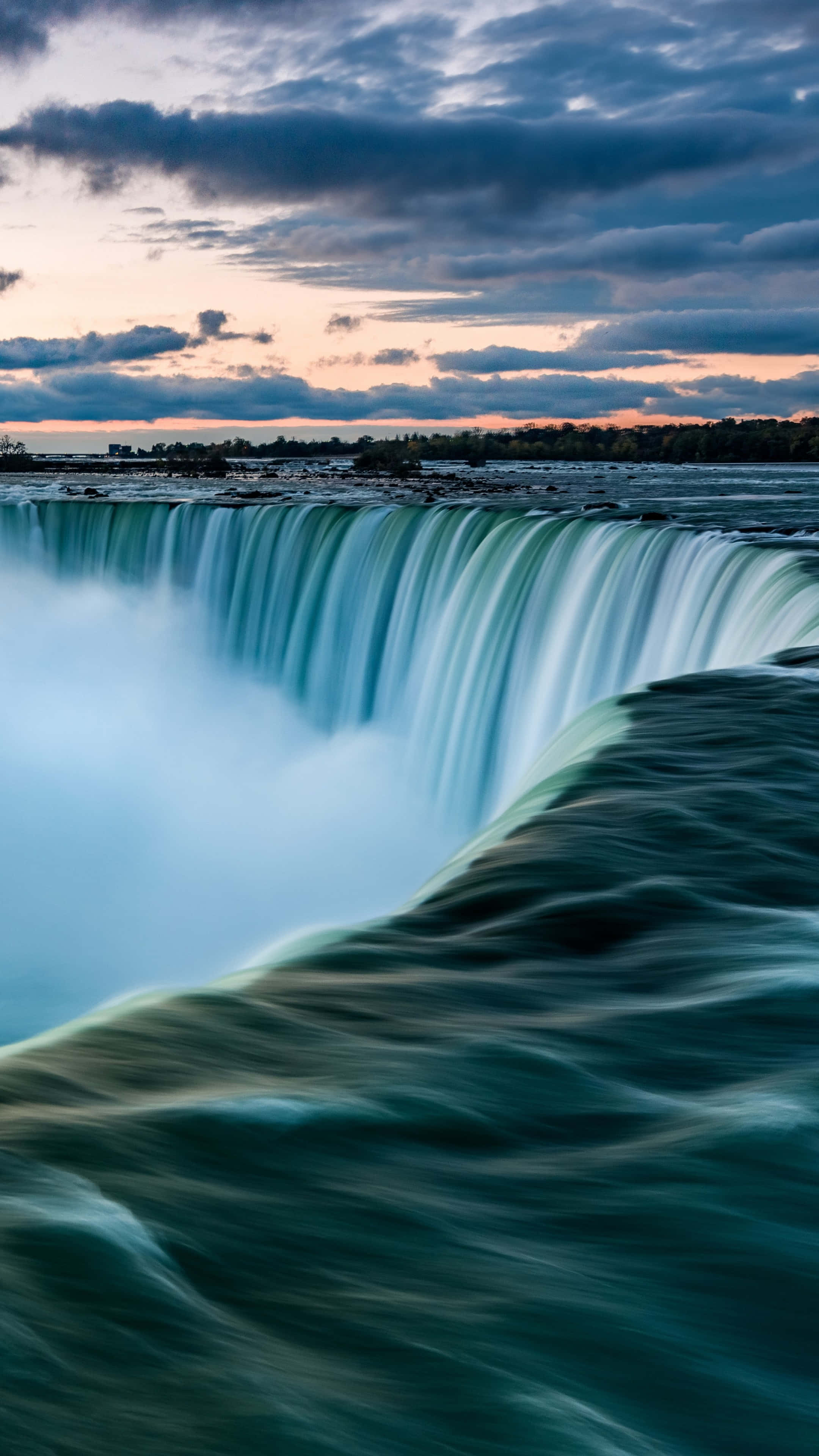 Niagara Falls 桌布 壁紙 — 一道壯麗的瀑布在粉紅色和藍色雲彩的戲劇性暮色天空下以慢動作傾瀉而下。