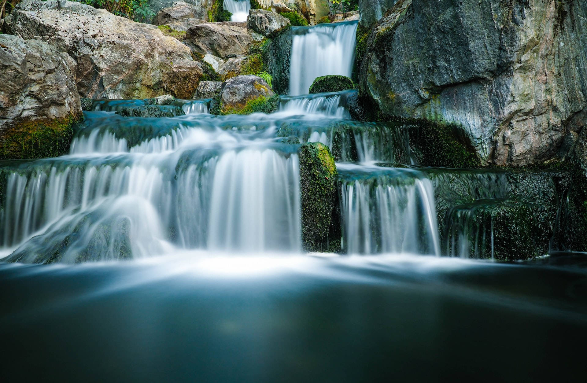 Moving Water 桌布 壁紙 — 一道寧靜的層疊瀑布從長滿苔蘚的岩石上傾瀉而下，流入平靜的水潭，水流順暢。