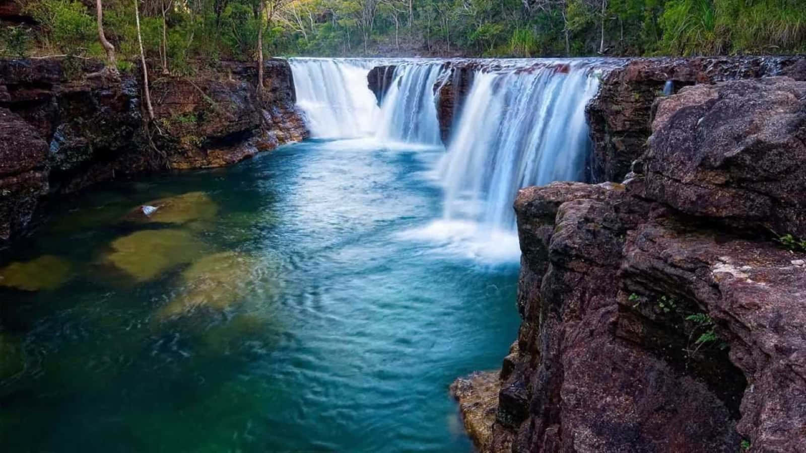 3d Waterfall 桌布 壁紙 — 一道寧靜的瀑布傾瀉而下，流入一個被崎嶇岩石和茂密綠色森林包圍的碧綠水池。