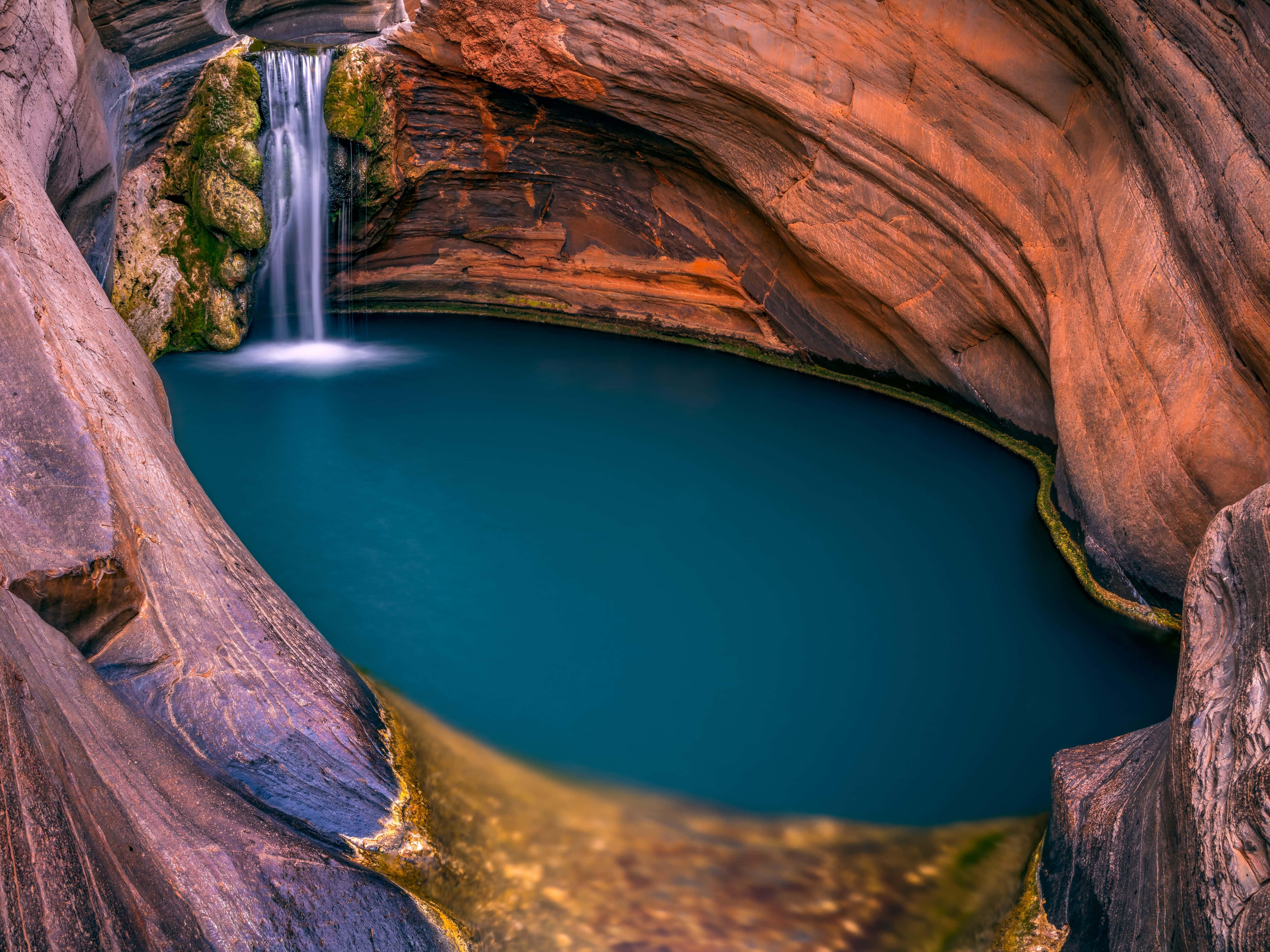 Blue Mountains National Park 桌布 壁紙 — 一道寧靜的瀑布傾瀉而下，流入一個深藍色的水池，水池坐落於由溫暖橙色和紫色岩石構成的彎曲峽谷中。