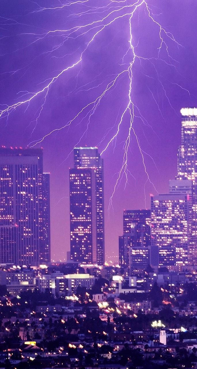 霓虹紫 iPhone 桌布 壁紙 — 一道巨大的紫色閃電劃過夜晚的城市天際線，下方是燈火通明的摩天大樓。