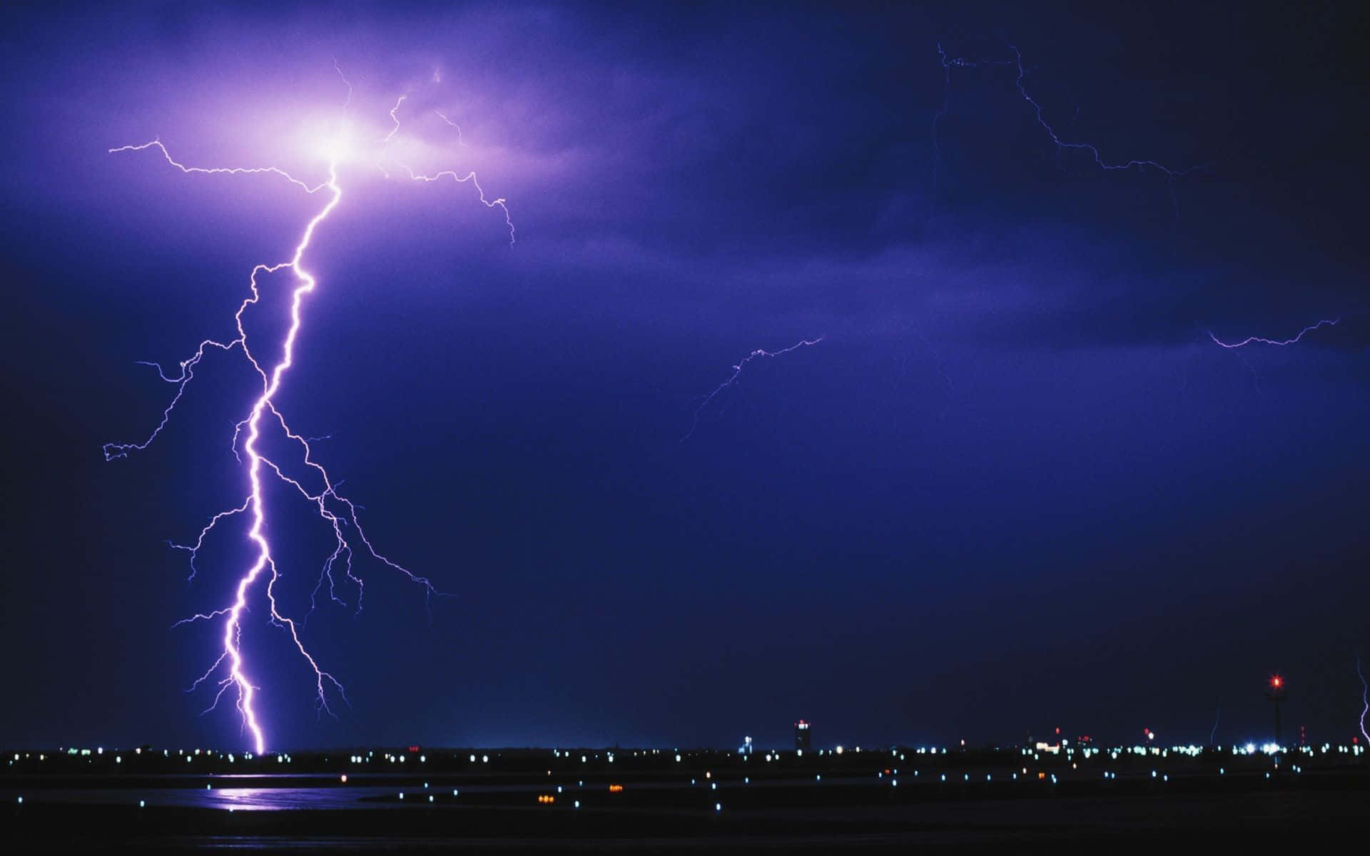 Thunderstorm 桌布 壁紙 — 一道巨大的紫色閃電在夜間擊中黑暗的城市景觀，照亮了雲層和遠處的燈光。