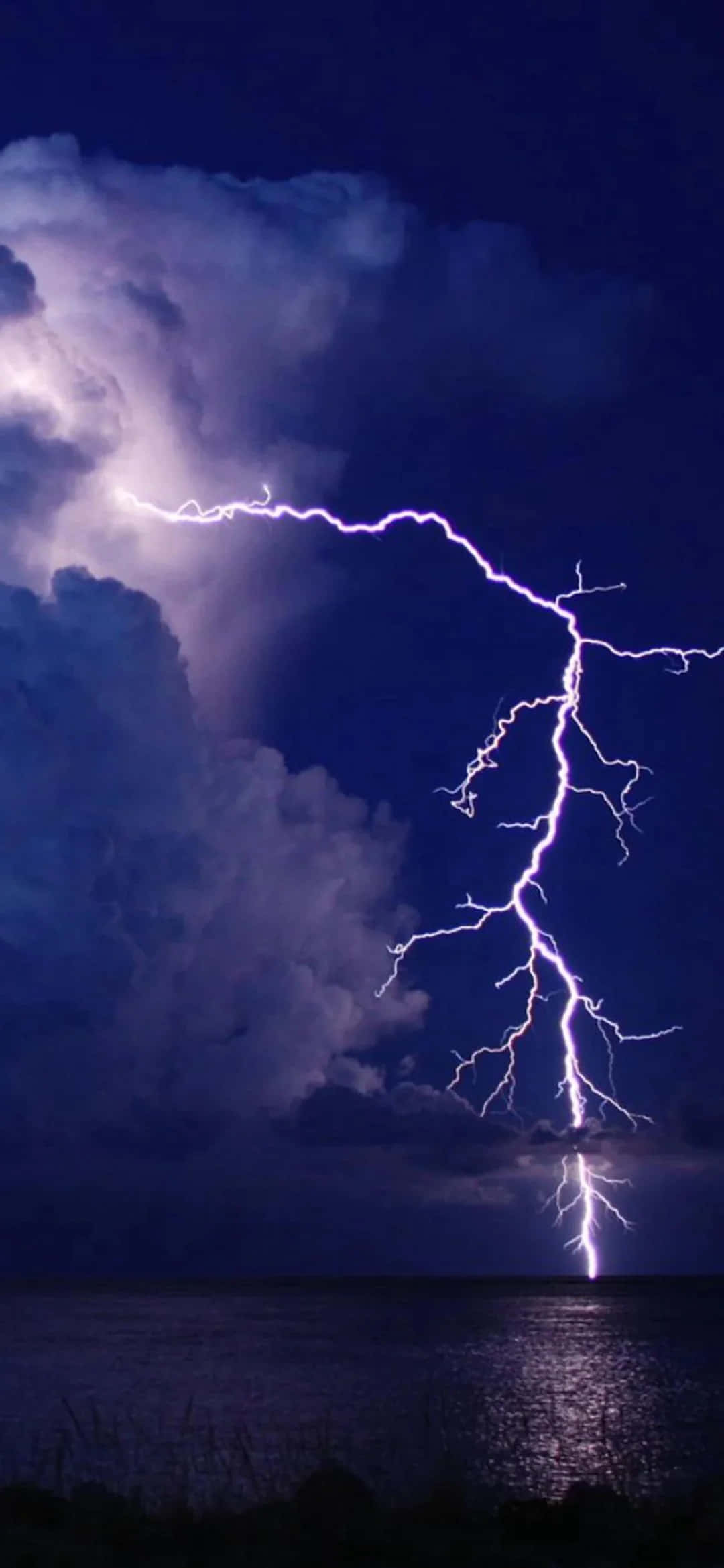 Lightning iPhone 桌布 壁紙 — 一道巨大的紫色閃電在黑暗水面上方的暴風雨夜空中分叉。