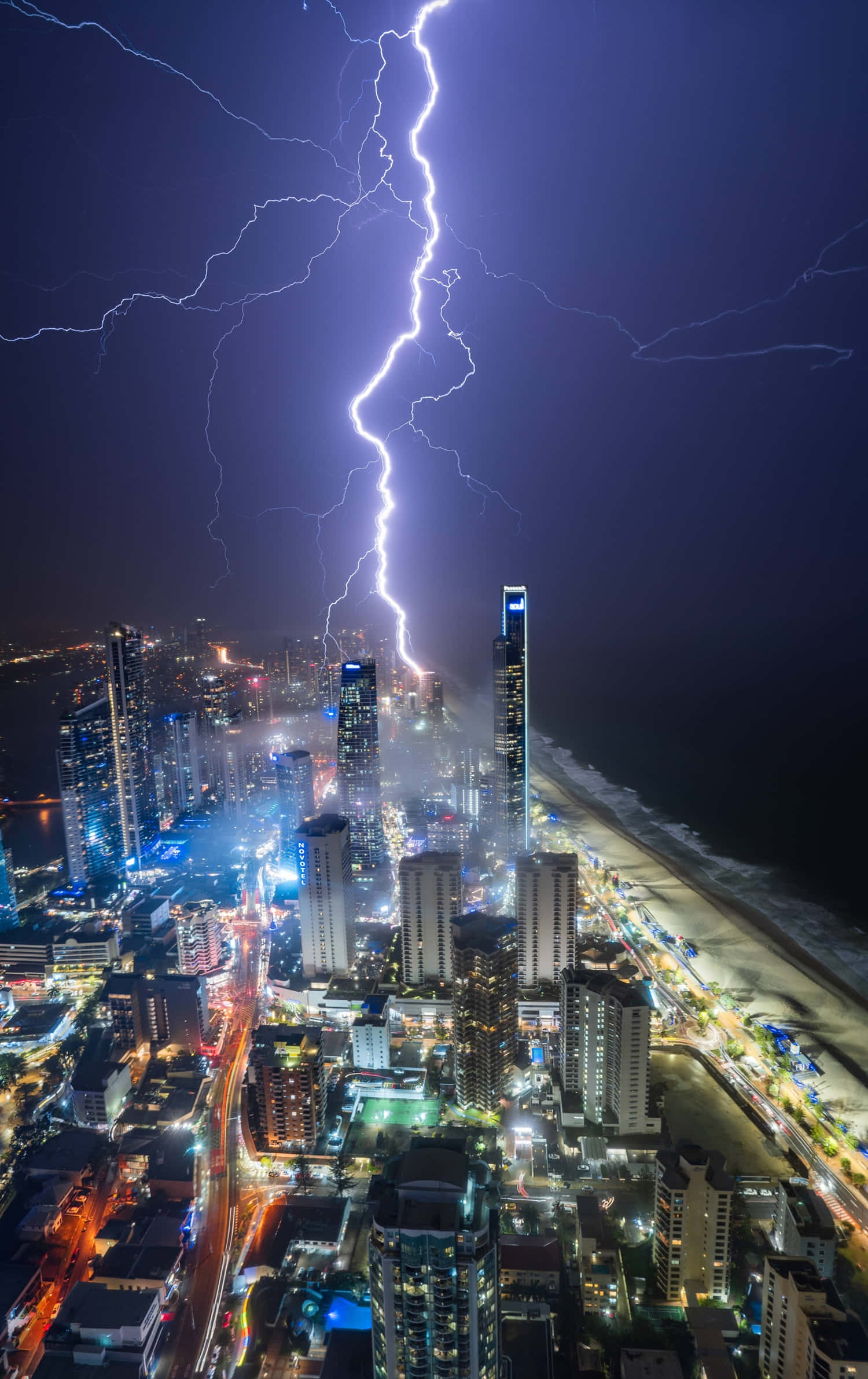 Stormy 桌布 壁紙 — 一道巨大的閃電劃過充滿活力的夜間海岸城市景觀，閃耀的摩天大樓和燈火通明的海灘。