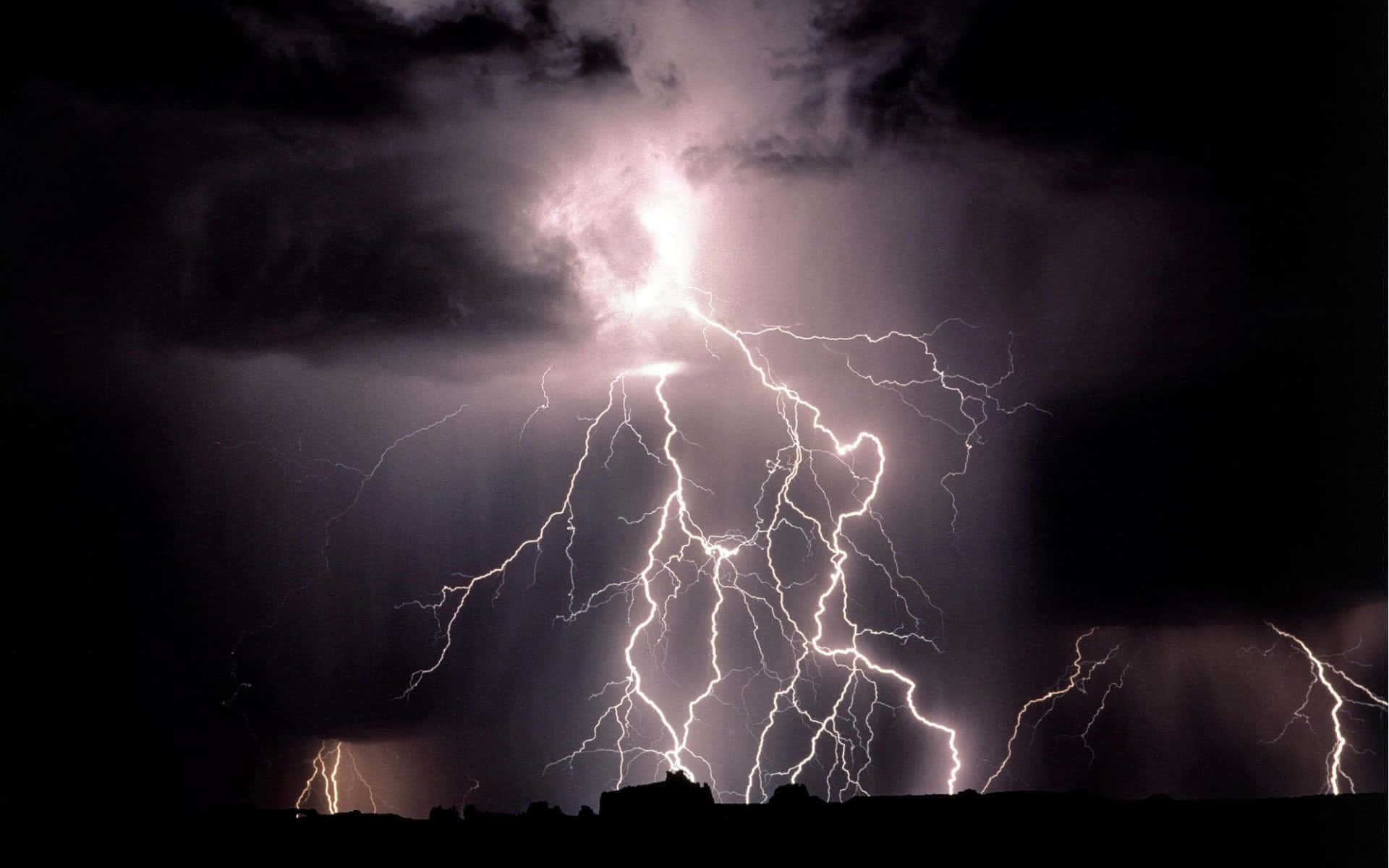 閃電 桌布 壁紙 — 一道巨大的閃電在暴風雨的夜空中分叉，下方是遠處山丘的黑暗輪廓。