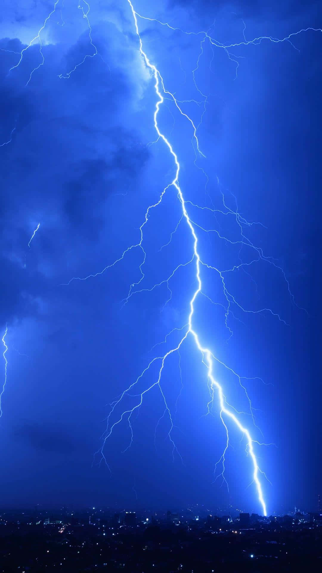 Lightning Bolt iPhone 桌布 壁紙 — 一道巨大的閃電在深藍色的暴風雨天空中分叉，劃過夜晚的城市天際線。