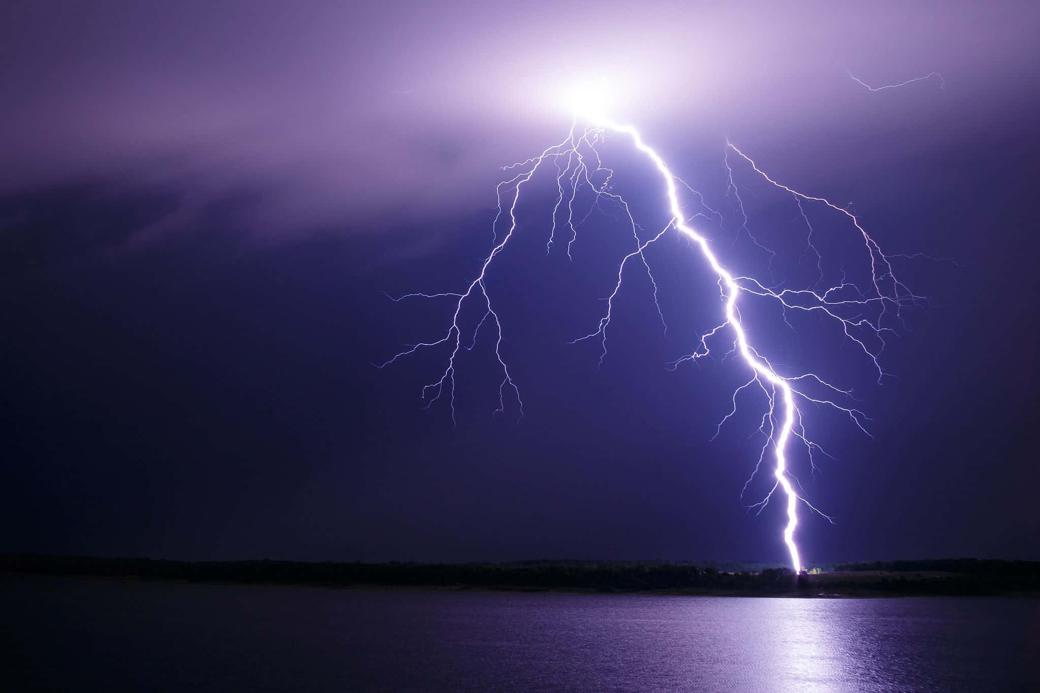 閃電 桌布 壁紙 — 一道巨大的閃電從暴風雨的紫色天空中擊中夜晚的黑暗湖泊。