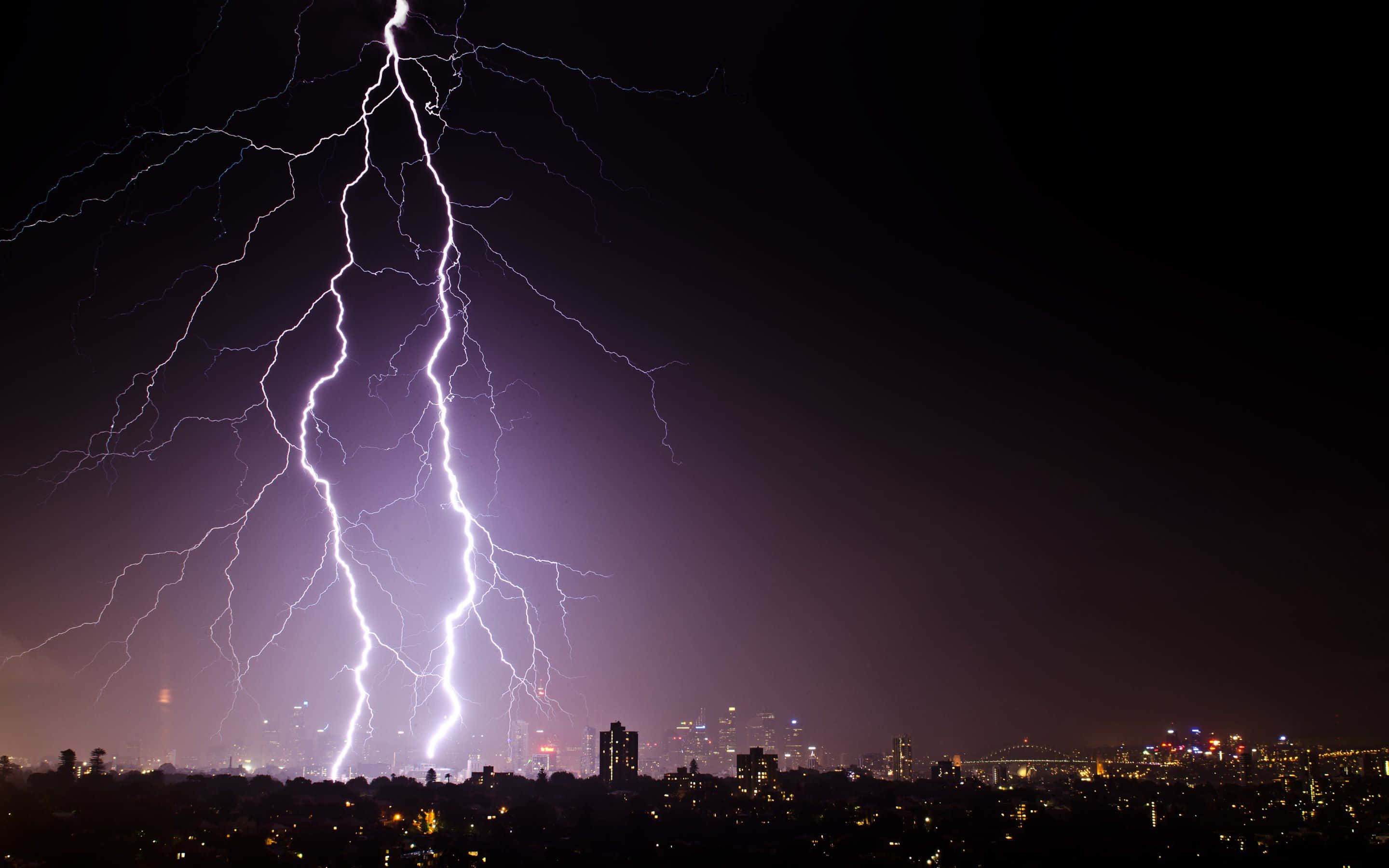thunder 桌布 壁紙 — 一道巨大的閃電照亮了暴風雨夜晚的天空，下方是燈火輝煌的廣闊城市景觀。