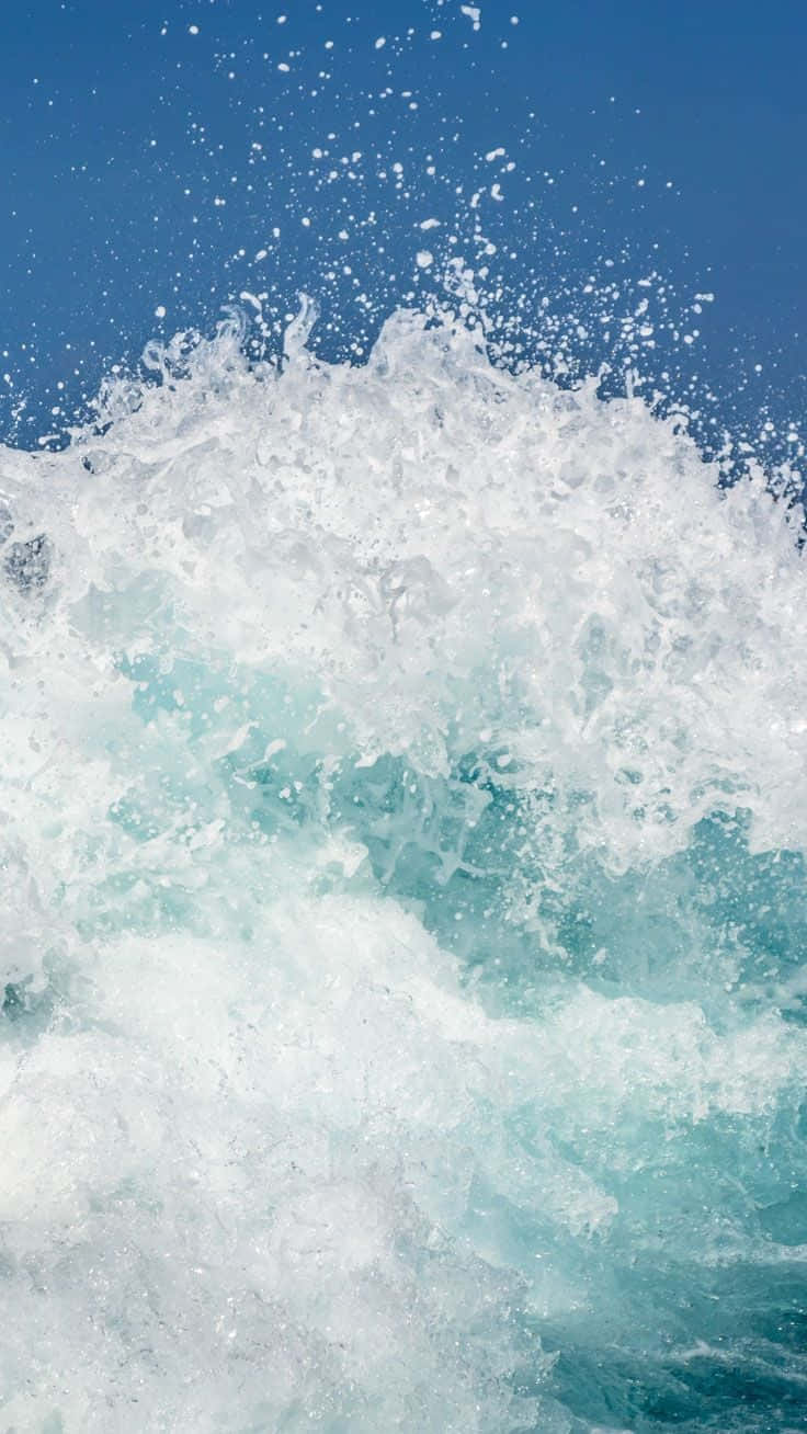 Wave 桌布 壁紙 — 一道強勁的海浪向上衝擊，噴出白色泡沫，映襯著清澈的藍天。
