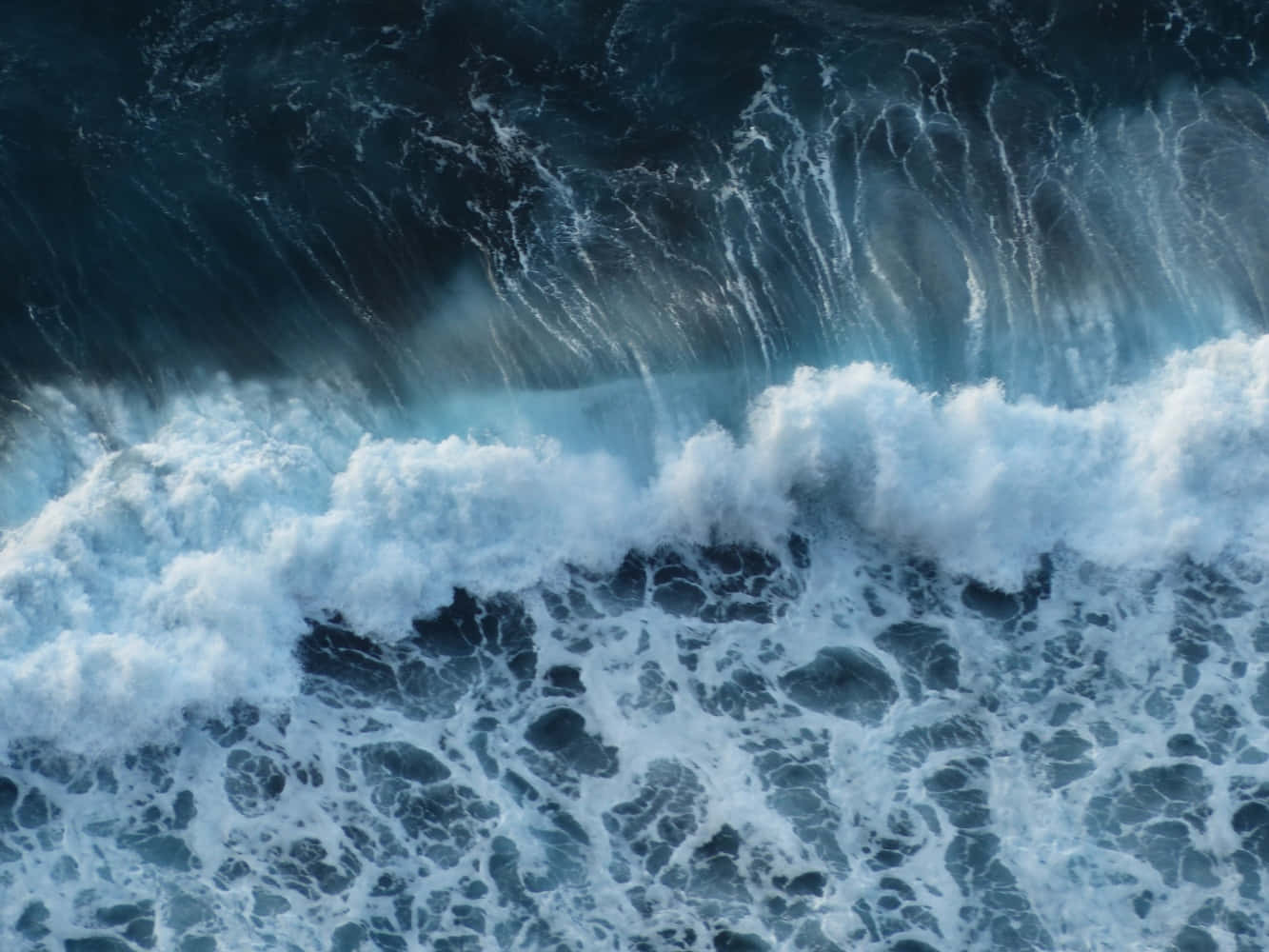 Wave 桌布 壁紙 — 一道強勁的海浪在戲劇性的航拍視角中，帶著白色泡沫撞擊深藍色的海水。