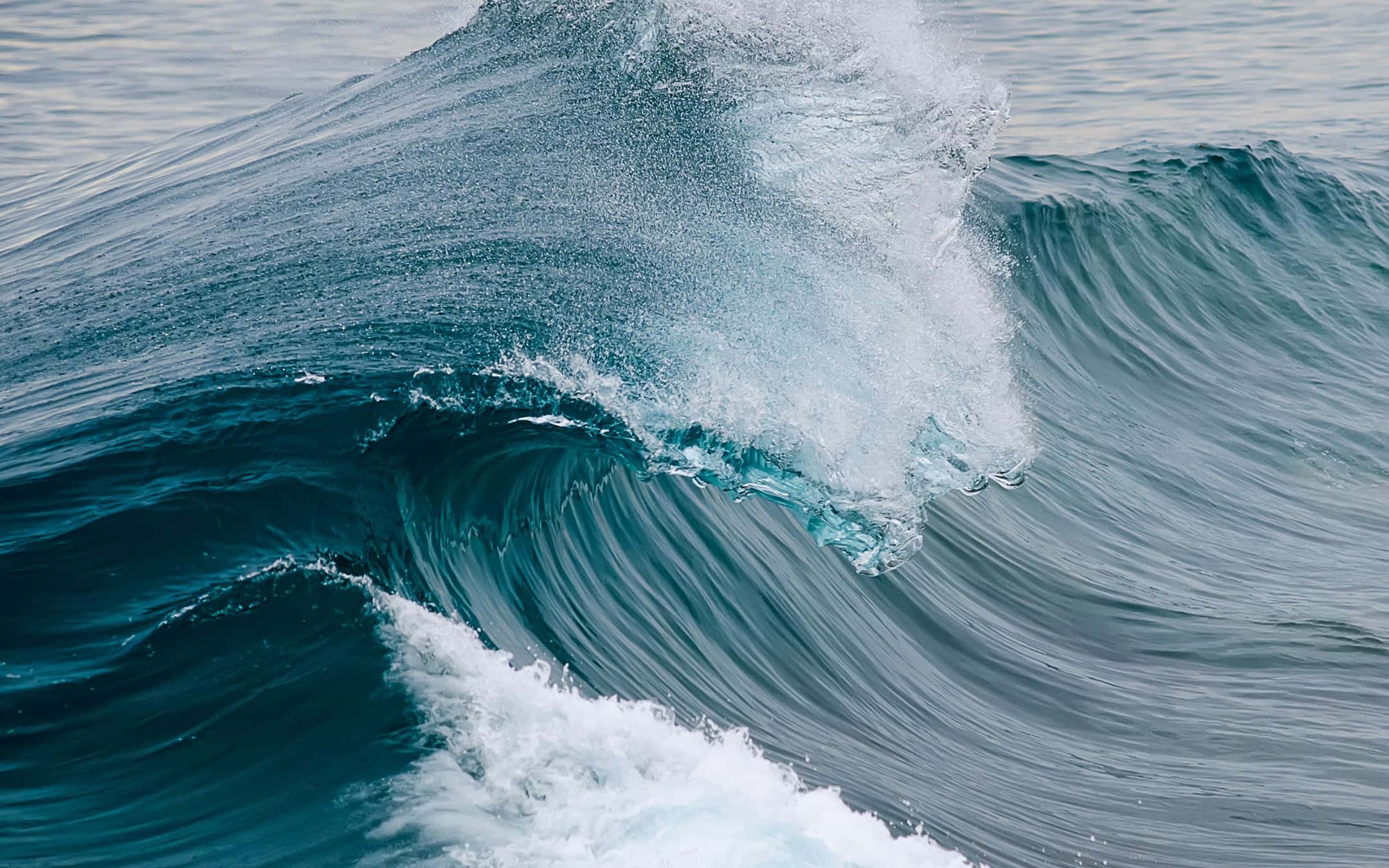 waves 桌布 壁紙 — 一道強勁的海浪捲起深藍綠色的海水和泡沫般的白色浪花，拍打著平靜的海面。
