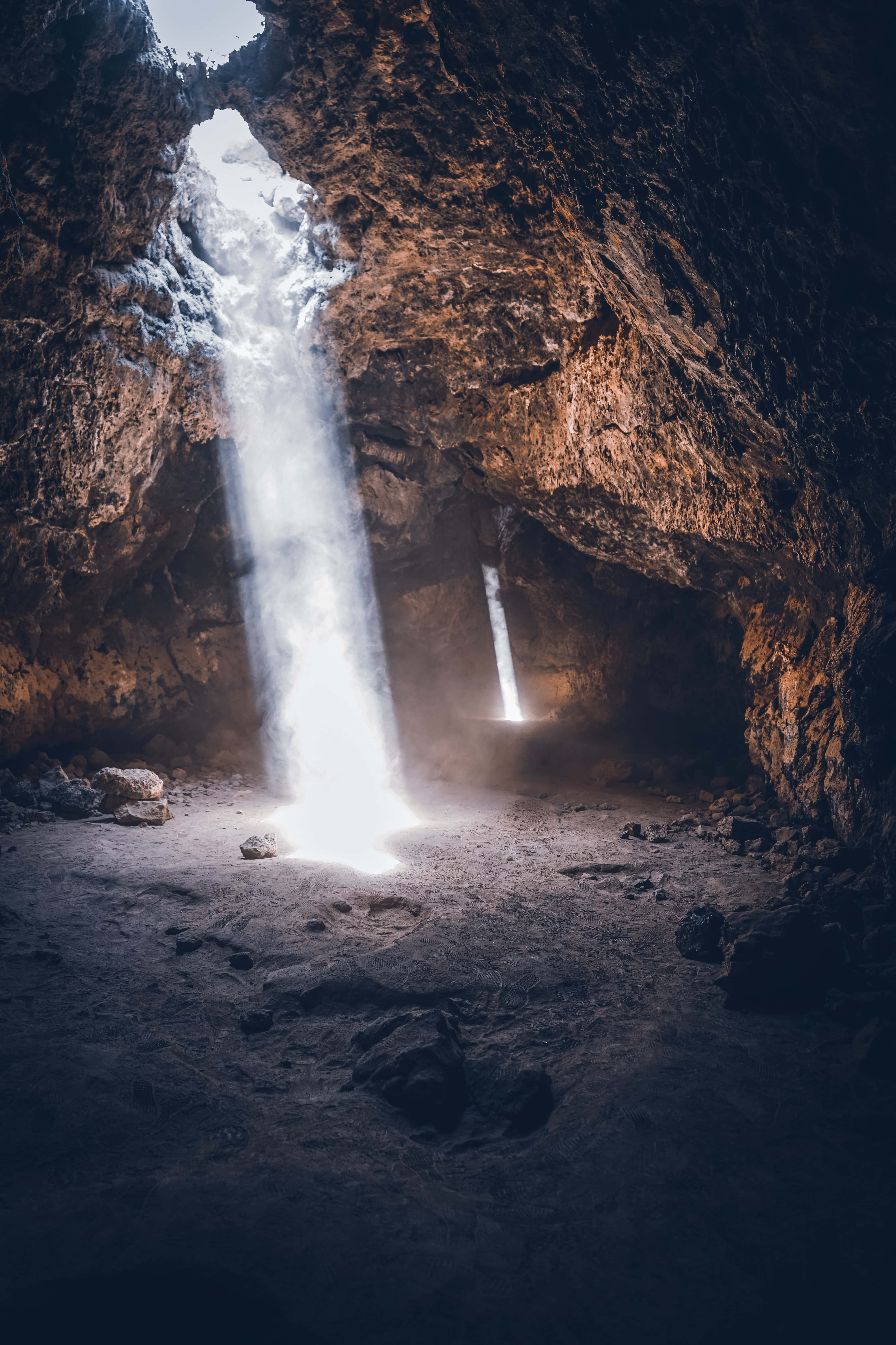 Cave 桌布 壁紙 — 一道強勁的瀑布傾瀉入一個黑暗的洞穴，洞穴被從上方射入的一束陽光照亮。