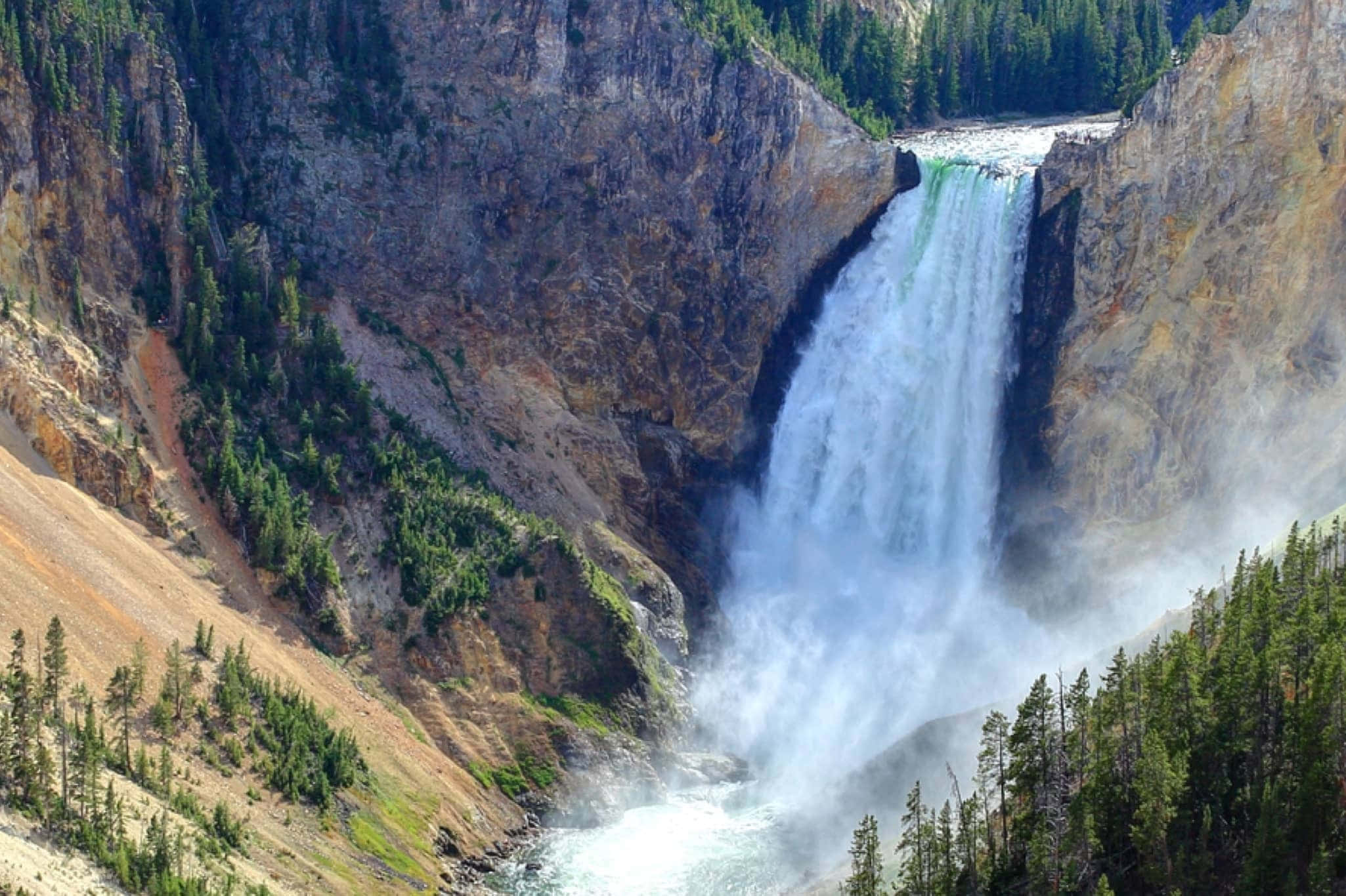 Yellowstone 桌布 壁紙 — 一道強勁的瀑布從崎嶇的懸崖傾瀉而下，流入被茂密常綠森林環繞的霧氣瀰漫的河流。