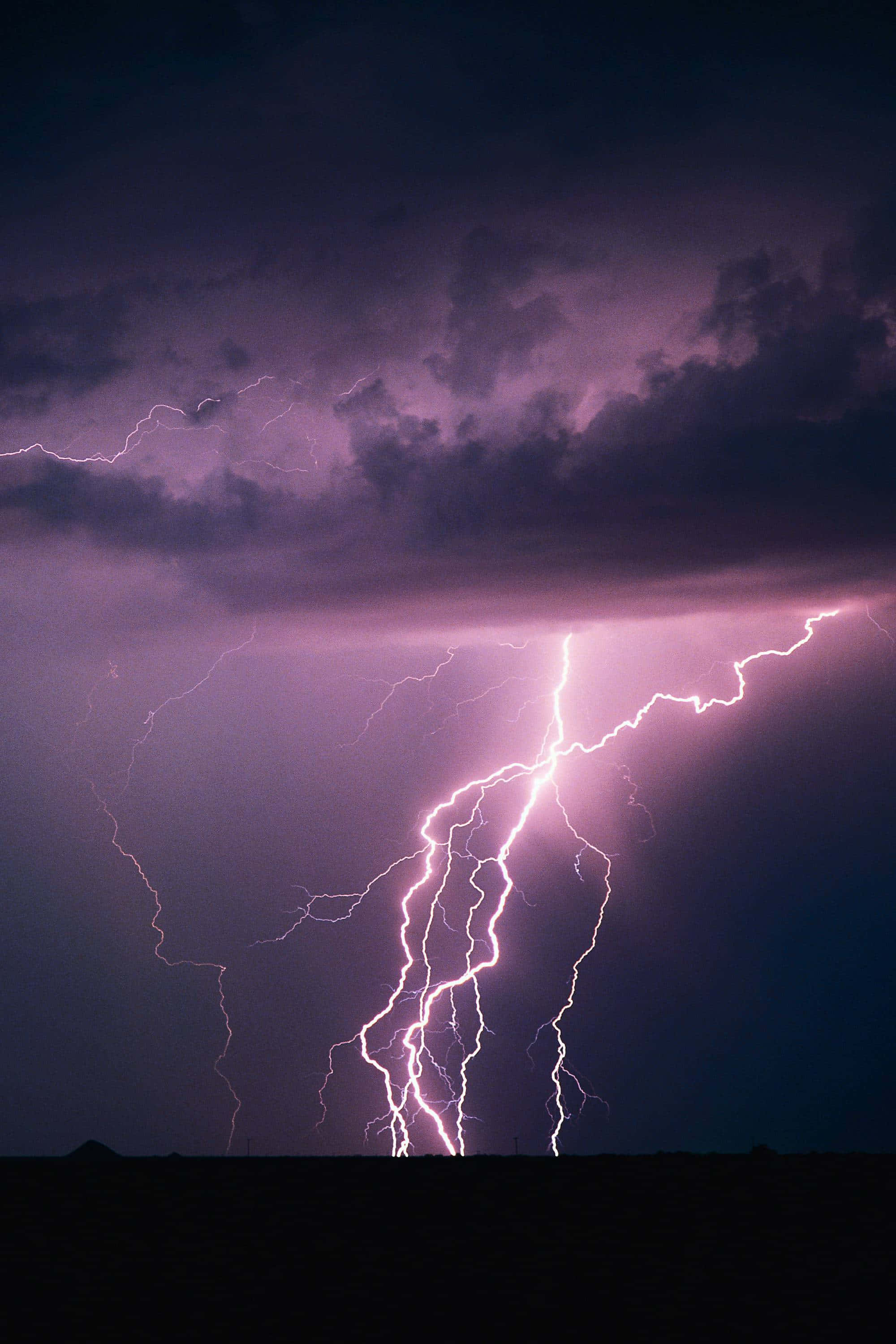 閃電 桌布 壁紙 — 一道強勁的紫色閃電在黑暗地平線上的暴風雨天空中分叉。