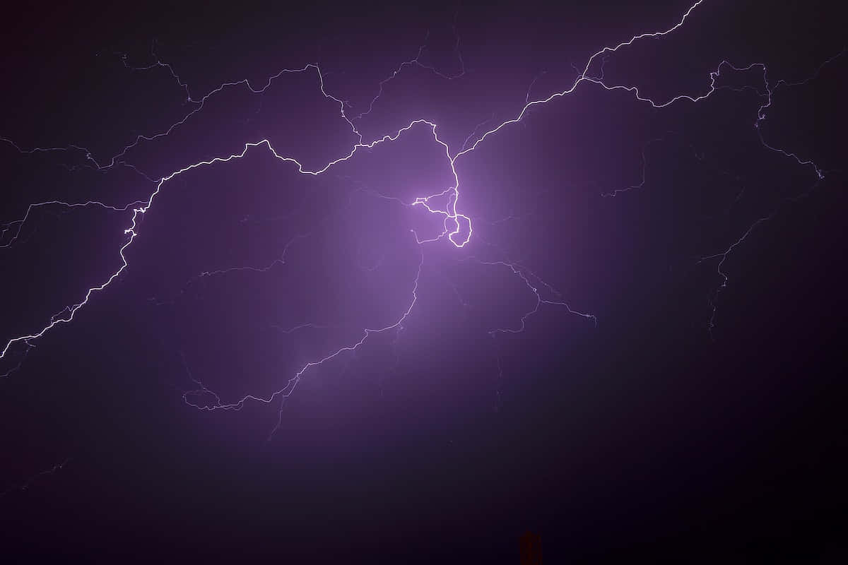 閃電 桌布 壁紙 — 一道強勁的紫色閃電在黑暗的暴風雨天空中分叉，呈現出戲劇性的自然景象。