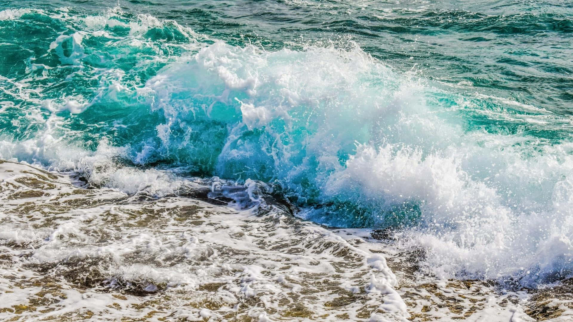 waves 桌布 壁紙 — 一道強勁的藍綠色海浪拍打岩石海岸，激起白色泡沫飛向空中。