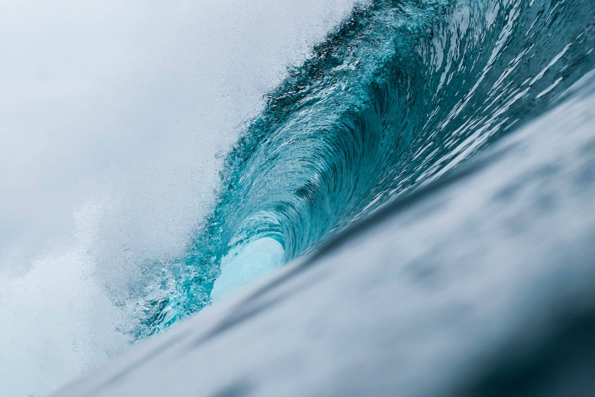 Wave 桌布 壁紙 — 一道強勁的藍綠色海浪捲成完美的筒狀，帶著白色泡沫飛濺，映襯著柔和的天色。