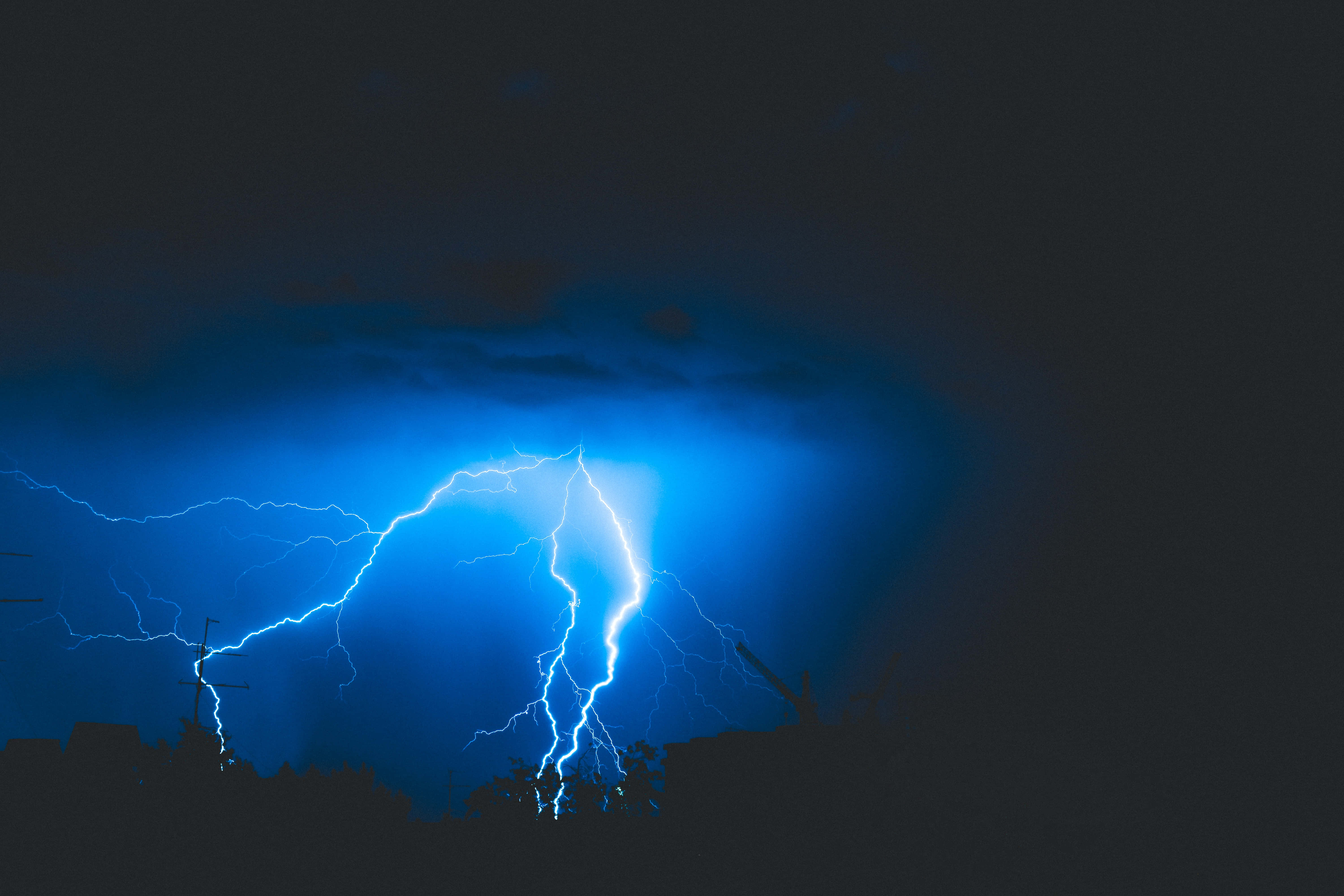 電力 桌布 壁紙 — 一道強勁的藍色閃電劃破漆黑的暴風雨夜空，下方是城市的剪影。