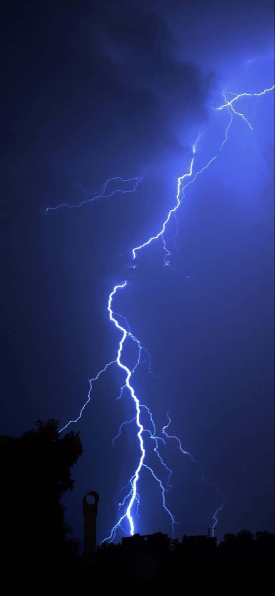 Cool Lightning 桌布 壁紙 — 一道強勁的藍色閃電戲劇性地在暴風雨夜空中分叉，下方是樹木和煙囪的剪影。