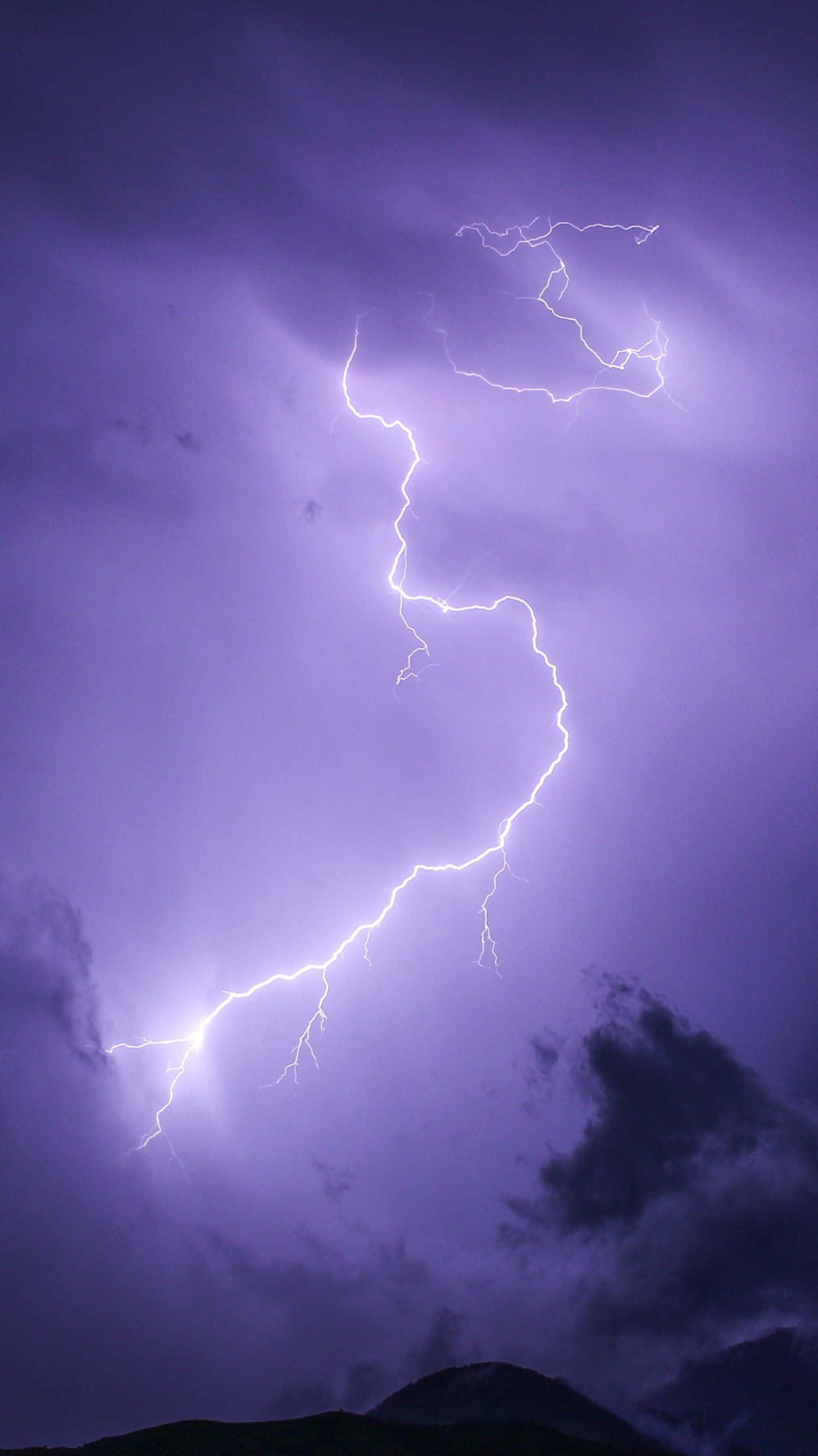 閃電 桌布 壁紙 — 一道強勁的鋸齒狀閃電在深紫色暴風雨天空中分叉，下方是黑暗的山脈輪廓。