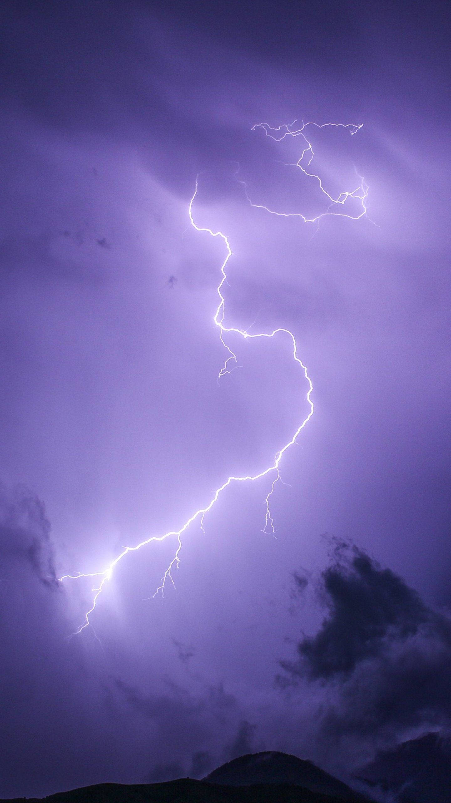 淡紫色 桌布 壁紙 — 一道強勁的鋸齒狀閃電在深紫色暴風雨天空中分叉，下方是黑暗的山脈輪廓。