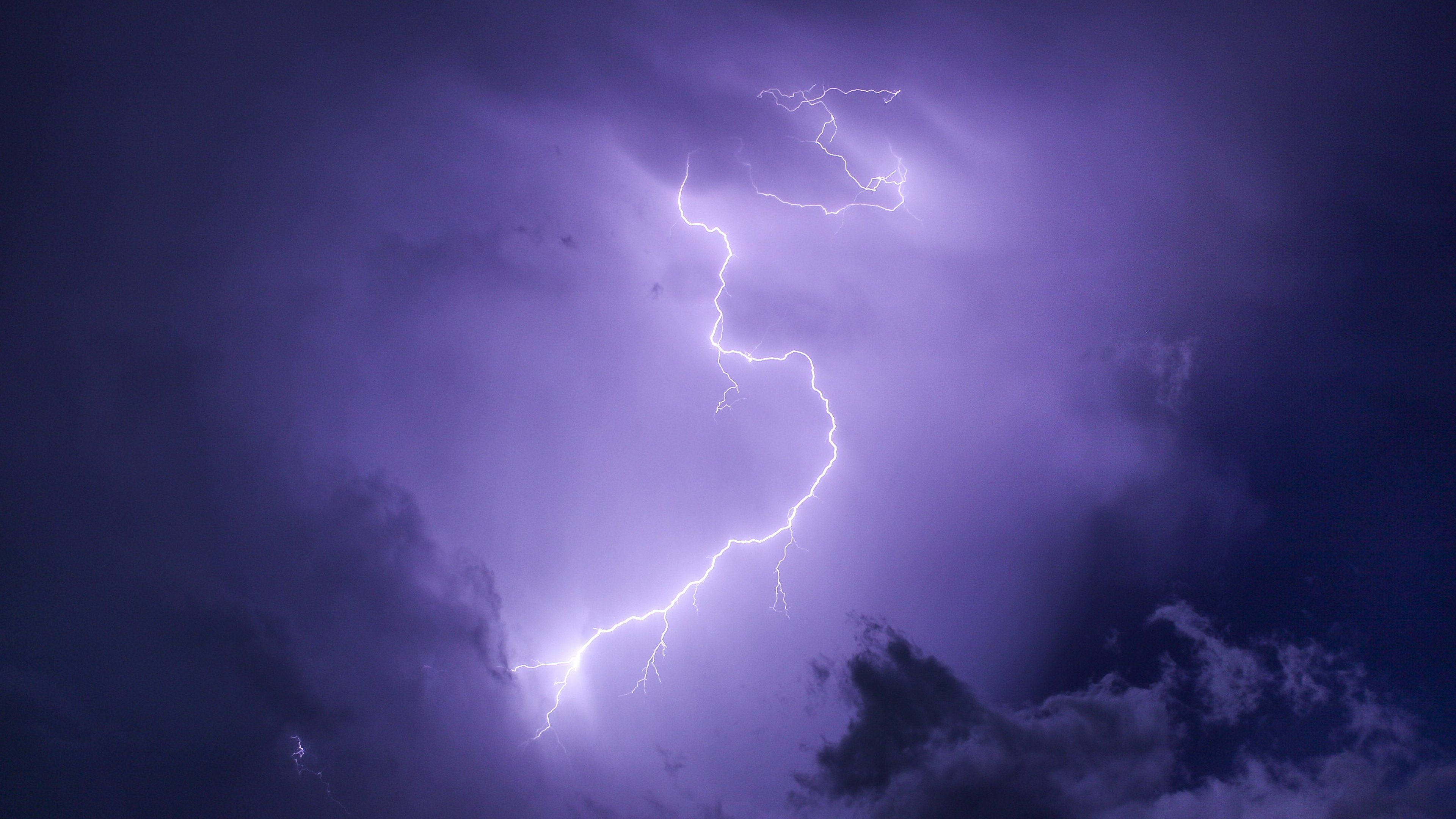 Aesthetic Lightning 桌布 壁紙 — 一道強勁的鋸齒狀閃電照亮了帶有烏雲的紫色暴風雨天空。
