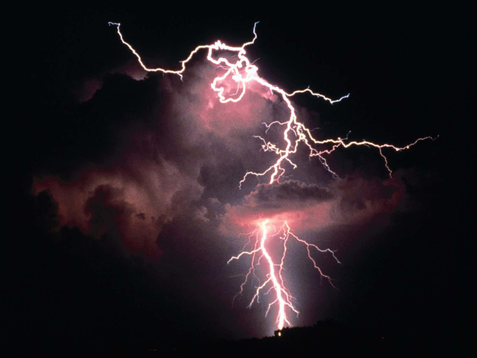 閃電 桌布 壁紙 — 一道強勁的閃電在黑暗的暴風雨天空中分叉，照亮了下方的粉紅色雲層。