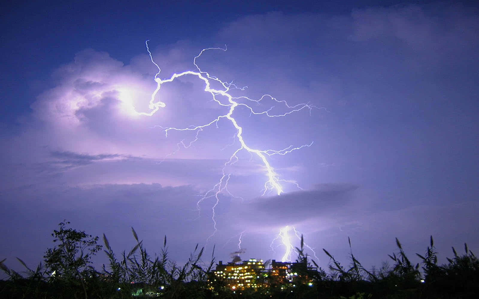 閃電 桌布 壁紙 — 一道強勁的閃電照亮了夜晚暴風雨紫色天空下的遠方城市景觀。
