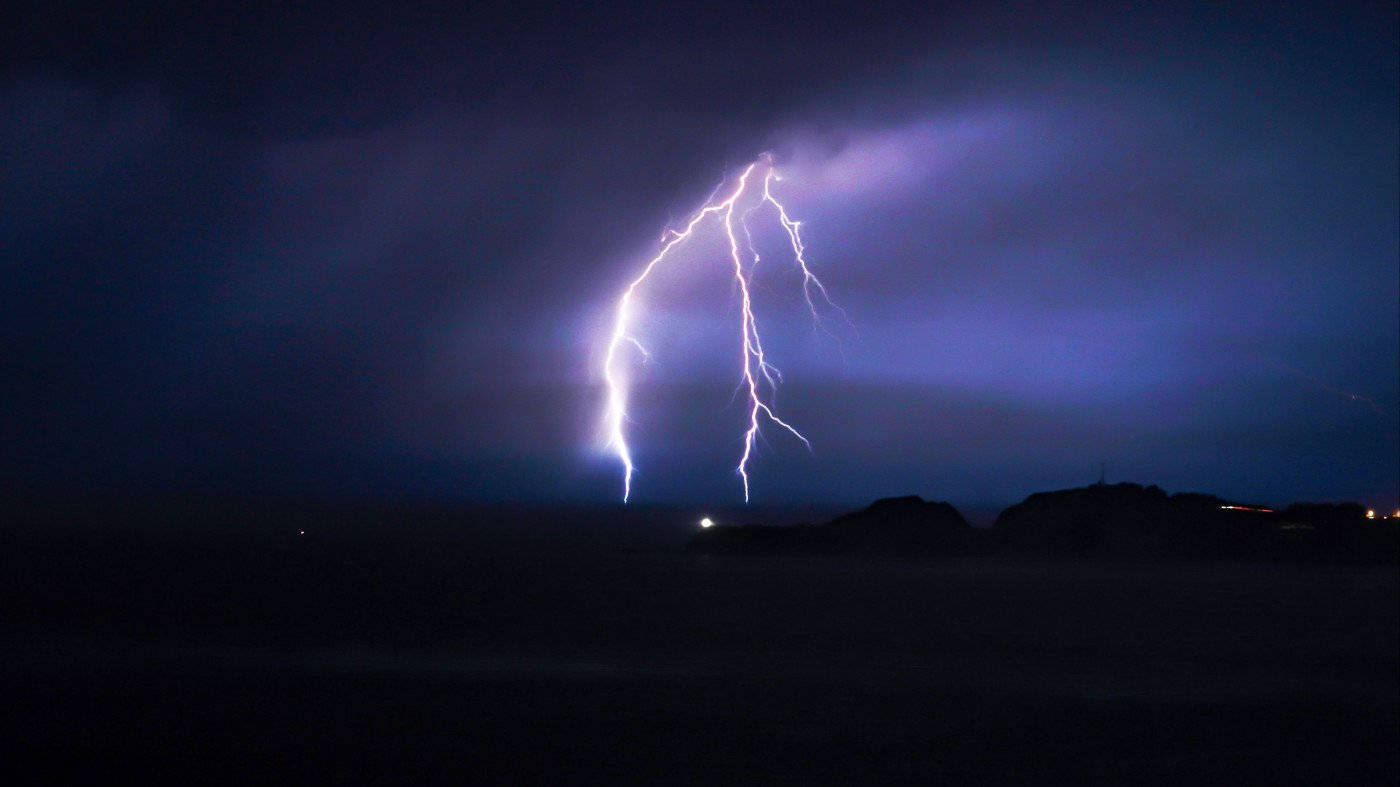 閃電 桌布 壁紙 — 一道強大的閃電在夜晚的黑暗暴風雨天空中分叉，掠過剪影般的風景。