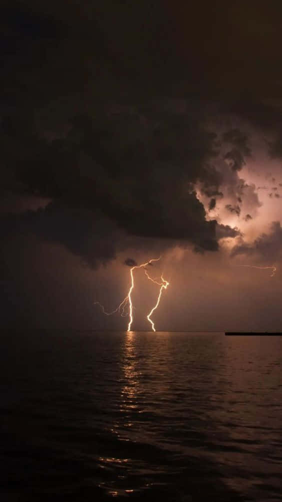 Cloud Aesthetic 桌布 壁紙 — 一道強大的閃電在夜間擊中海洋，在暴風雲下的黑暗海面上投射出金色倒影。
