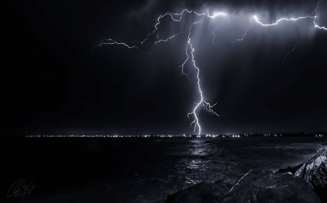 閃電 桌布 壁紙 — 一道強大的閃電在夜間擊中黑暗的海洋，照亮地平線上遙遠的城市燈光。